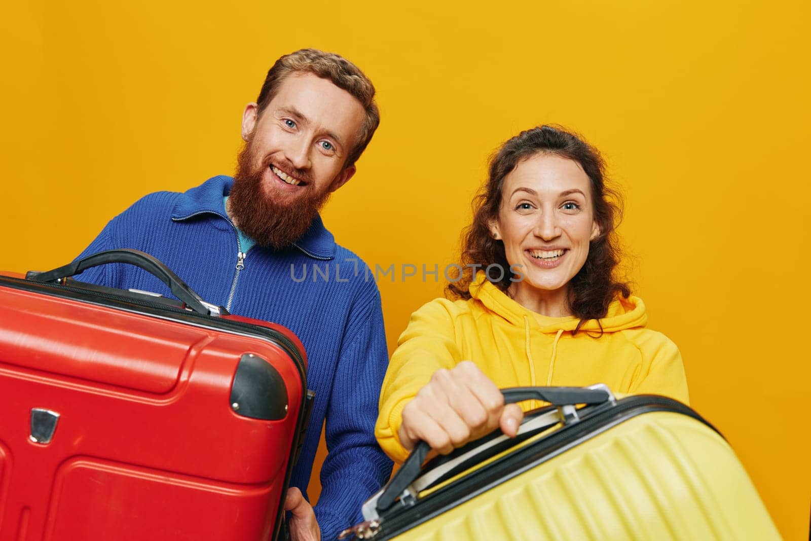 Woman and man smiling, suitcases in hand with yellow and red suitcase smiling merrily and crooked, yellow background, going on a trip, family vacation trip, newlyweds. by SHOTPRIME