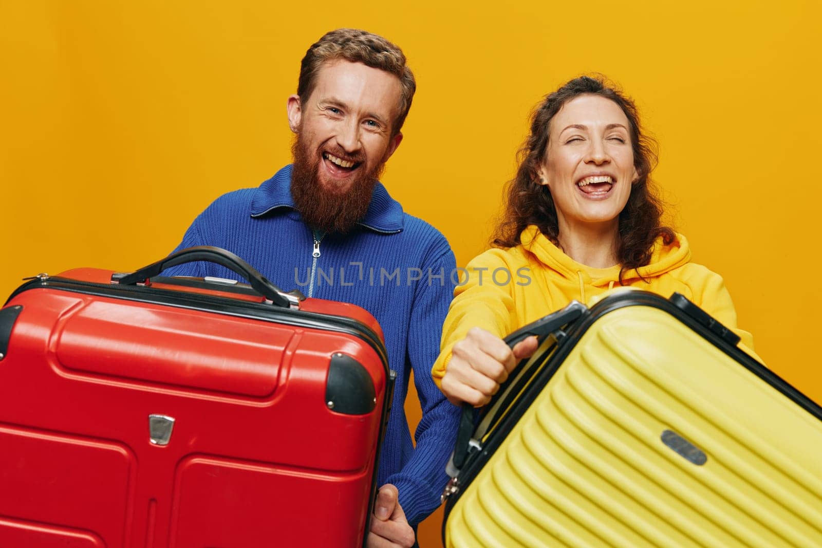 Woman and man smiling, suitcases in hand with yellow and red suitcase smiling merrily and crooked, yellow background, going on a trip, family vacation trip, newlyweds. High quality photo