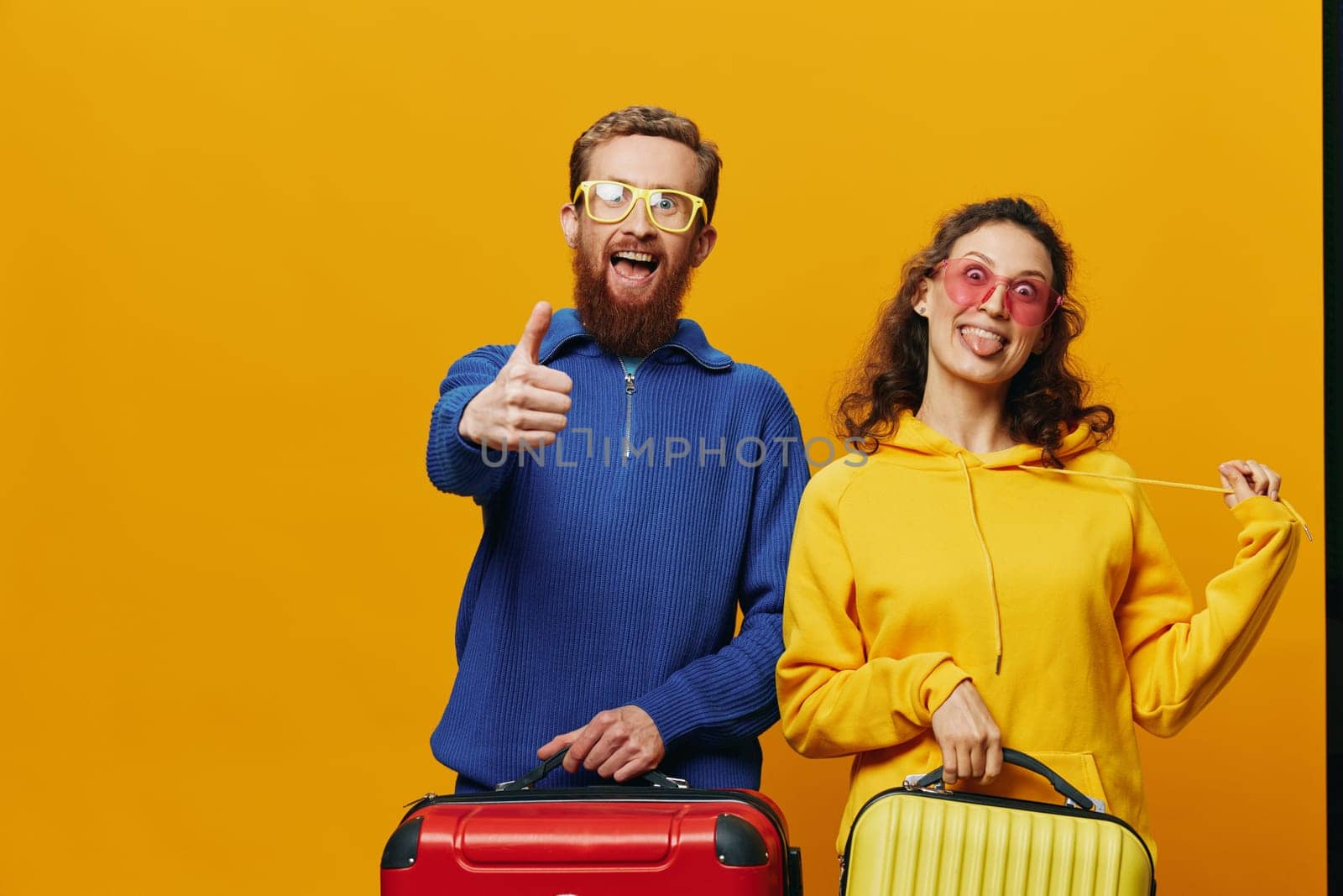 Woman and man smiling, suitcases in hand with yellow and red suitcase smiling merrily and crooked, yellow background, going on a trip, family vacation trip, newlyweds. High quality photo