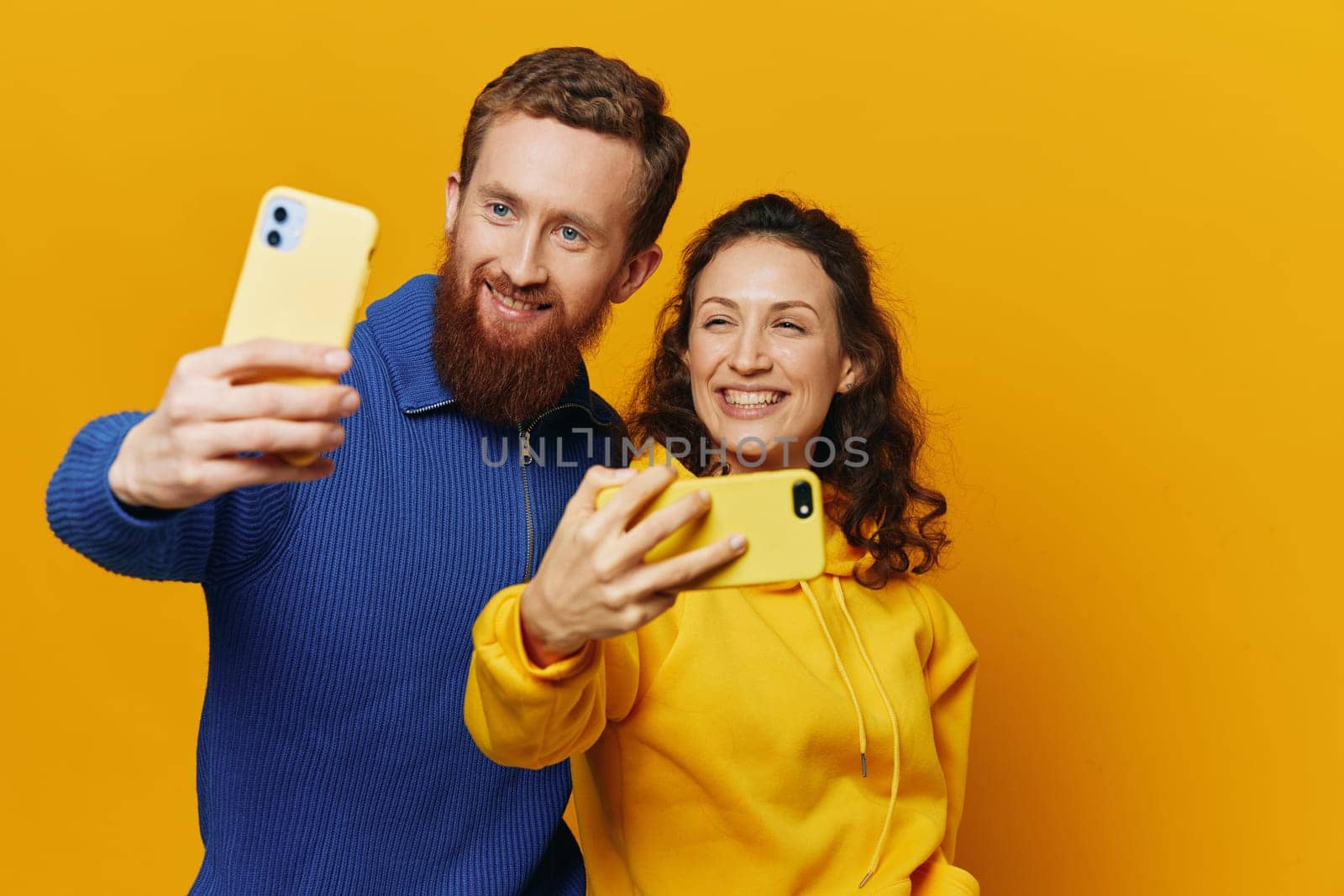 Man and woman couple smiling merrily with phone in hand social media viewing photos and videos, on yellow background, symbols signs and hand gestures, family freelancers. High quality photo