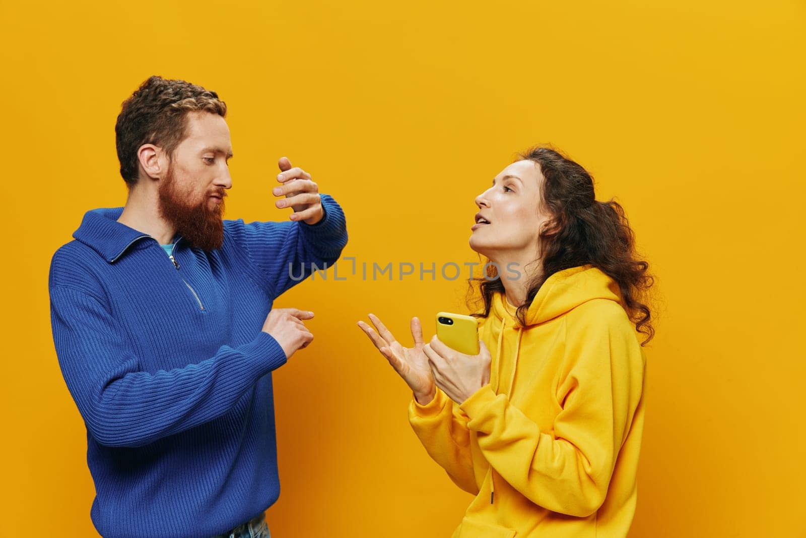 Woman and man cheerful couple with phones in hand social networking and communication crooked smile fun and fight, in yellow background. The concept of real family relationships, freelancers, work online. High quality photo