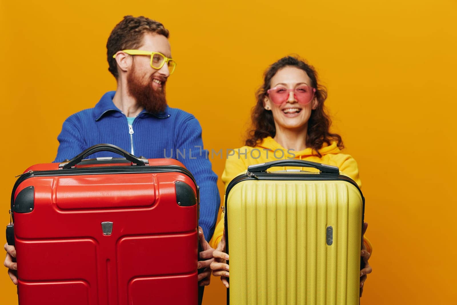 Woman and man smiling, suitcases in hand with yellow and red suitcase smiling merrily and crooked, yellow background, going on a trip, family vacation trip, newlyweds. High quality photo