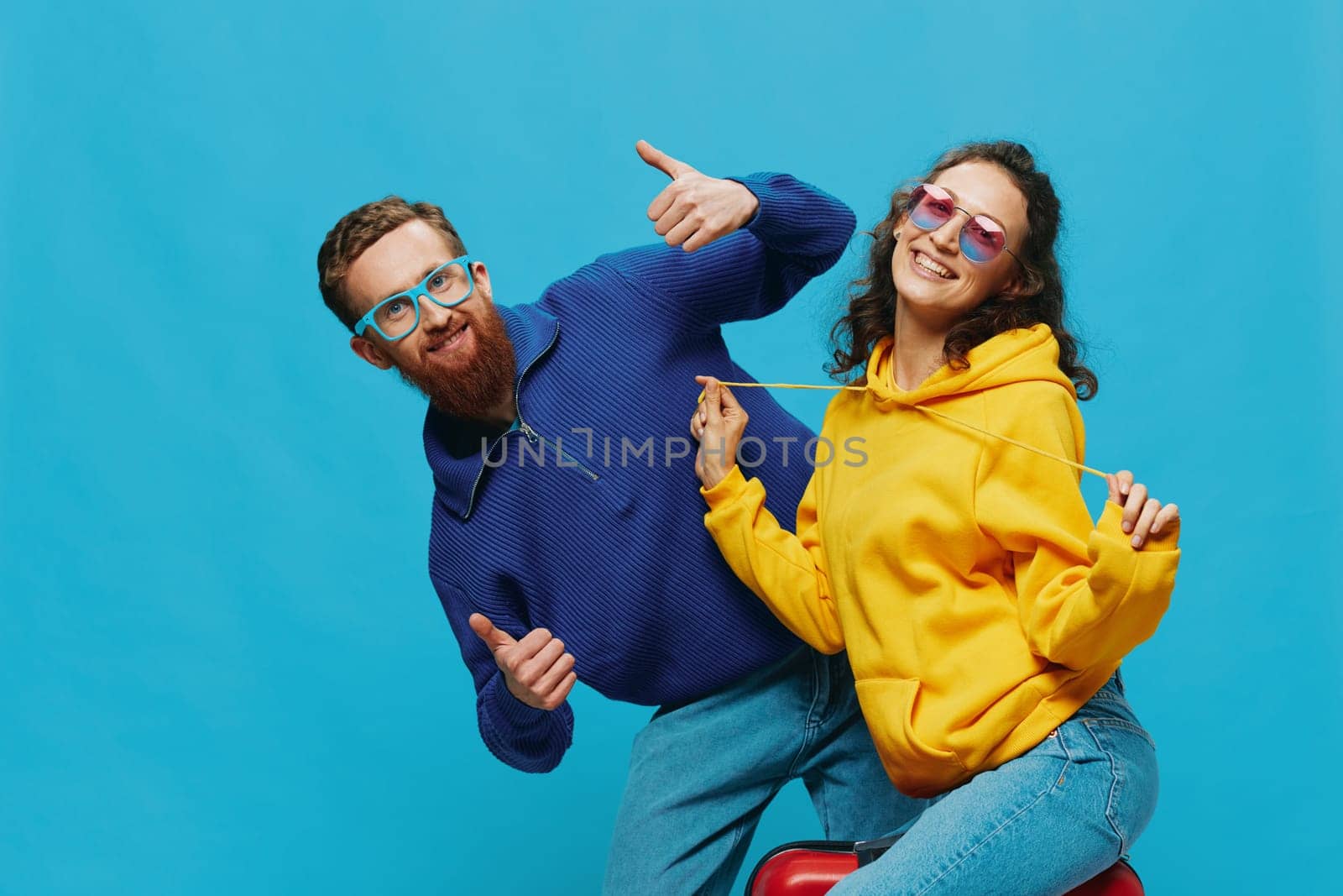 Woman and man smile sitting on suitcase with red suitcase smile, on blue background, packing for trip, family vacation trip. High quality photo