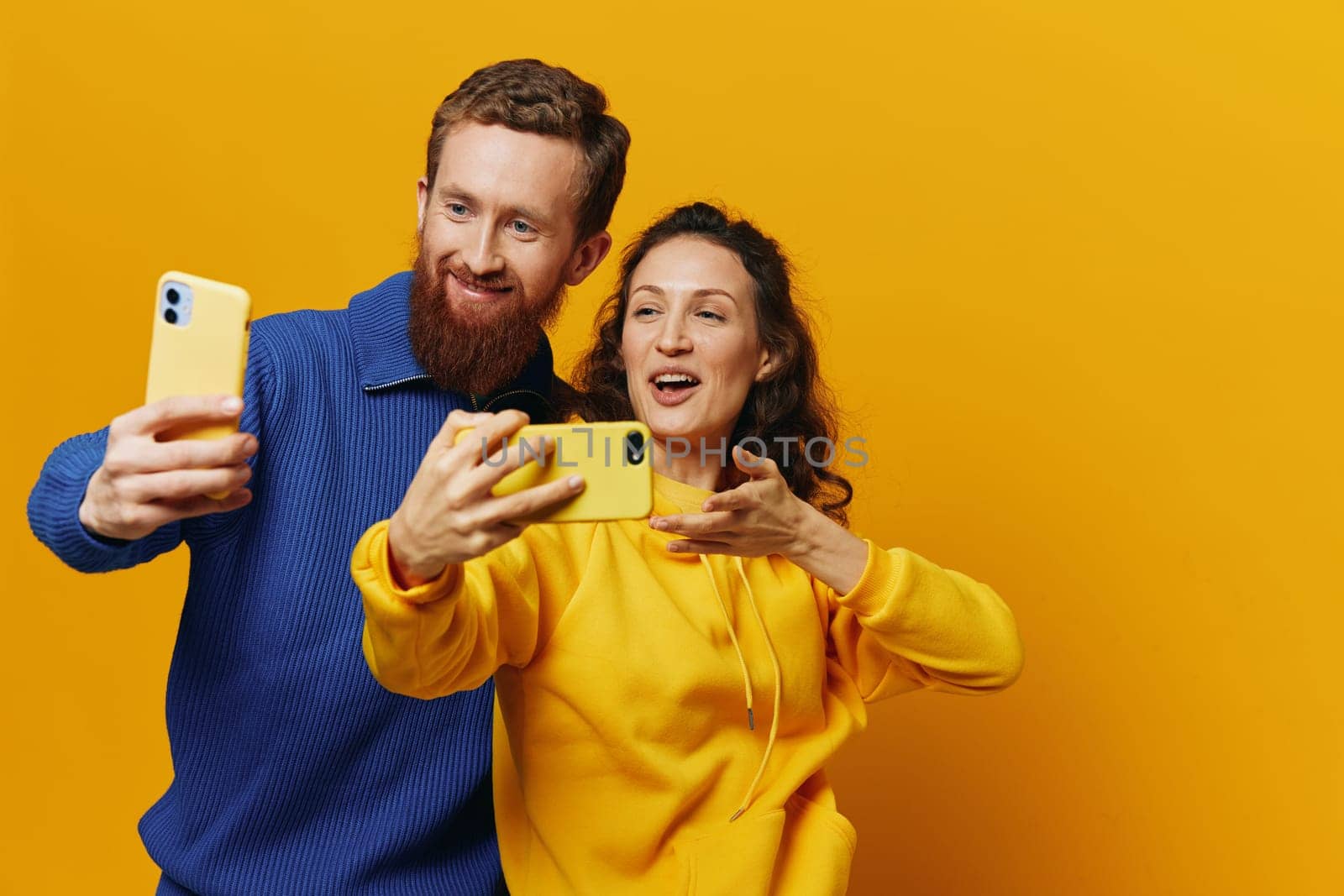 Man and woman couple smiling merrily with phone in hand social media viewing photos and videos, on yellow background, symbols signs and hand gestures, family freelancers. by SHOTPRIME