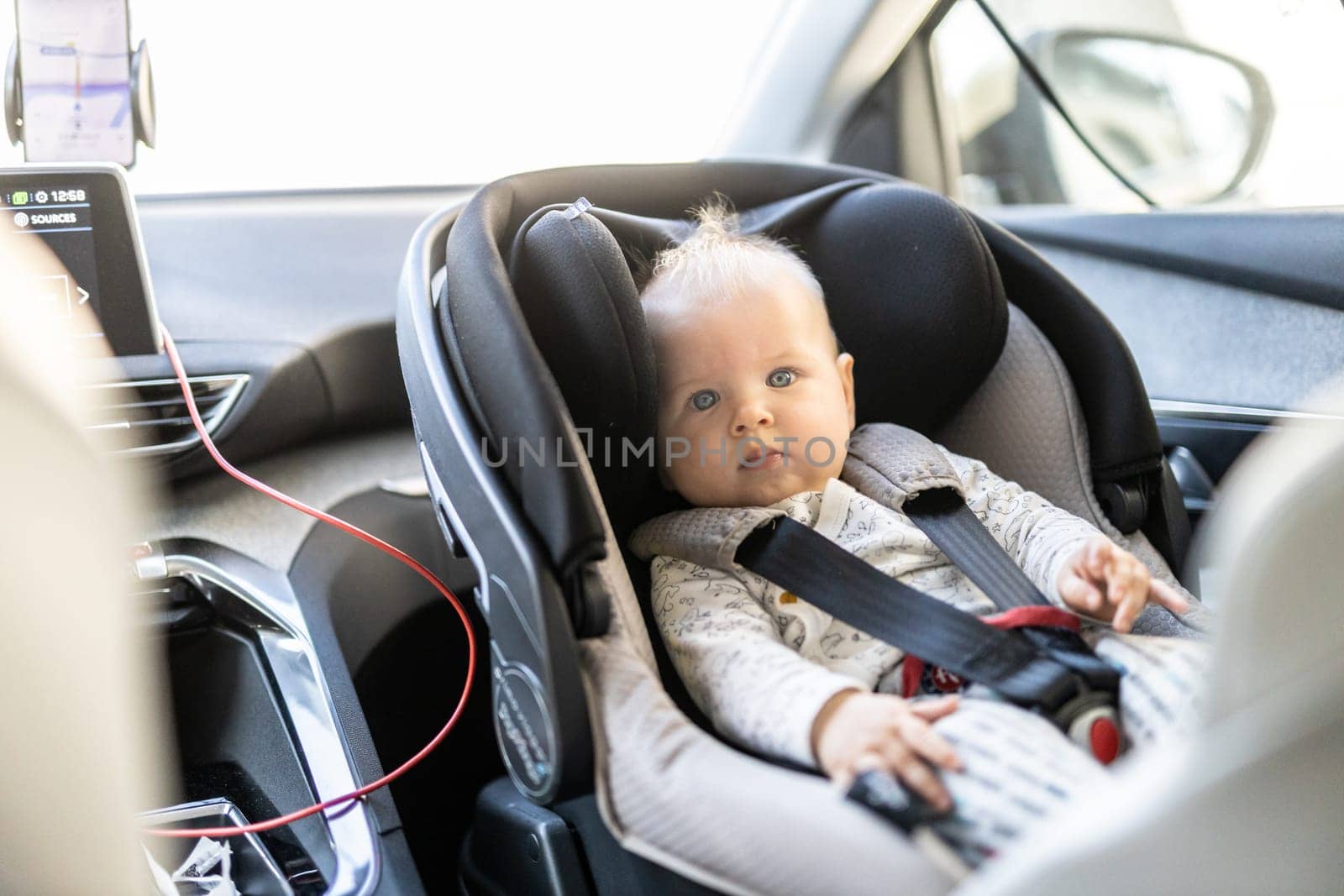 Cute little baby boy strapped into infant car seat in passenger compartment during car drive