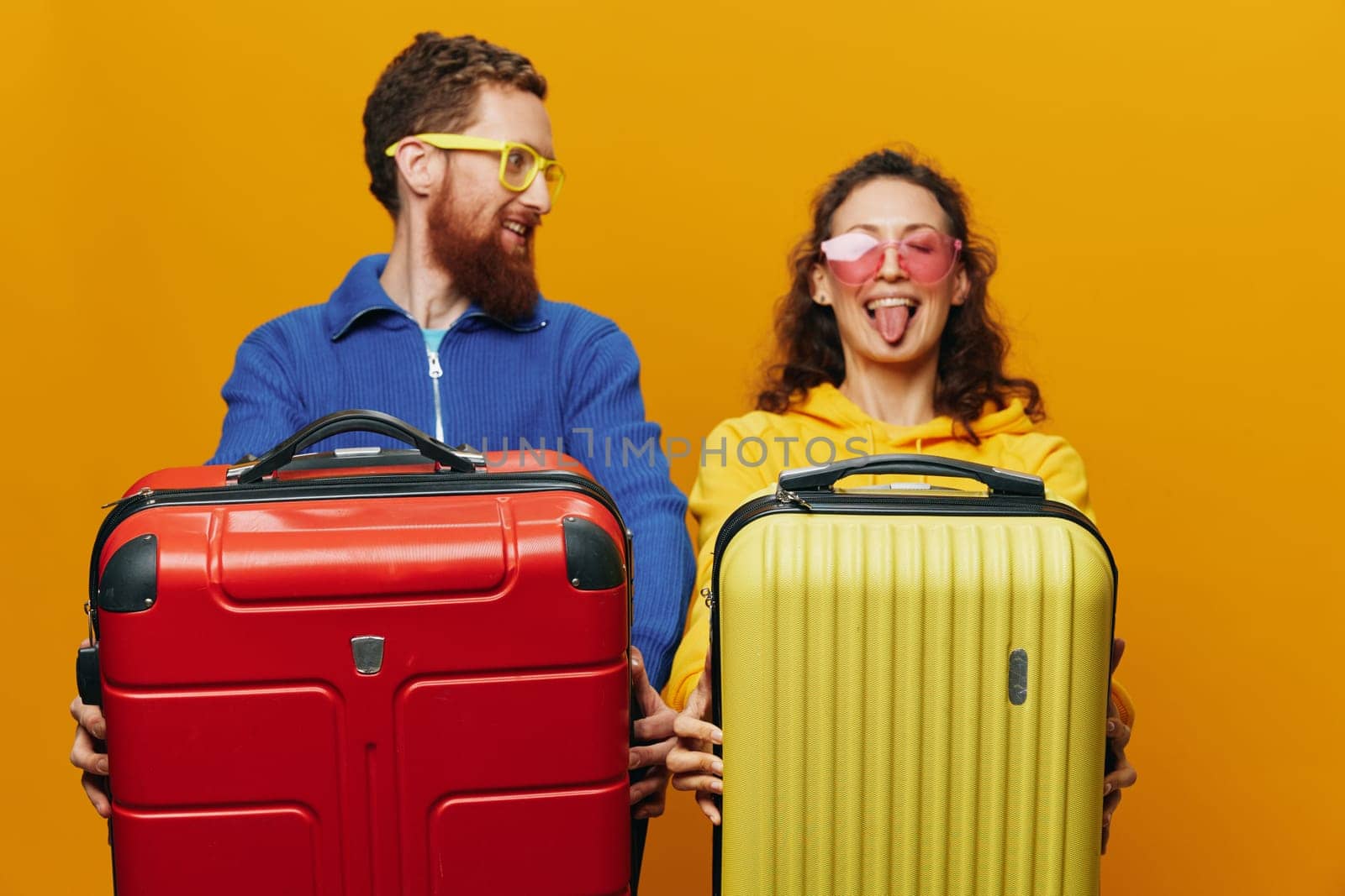 Woman and man smiling, suitcases in hand with yellow and red suitcase smiling merrily and crooked, yellow background, going on a trip, family vacation trip, newlyweds. by SHOTPRIME