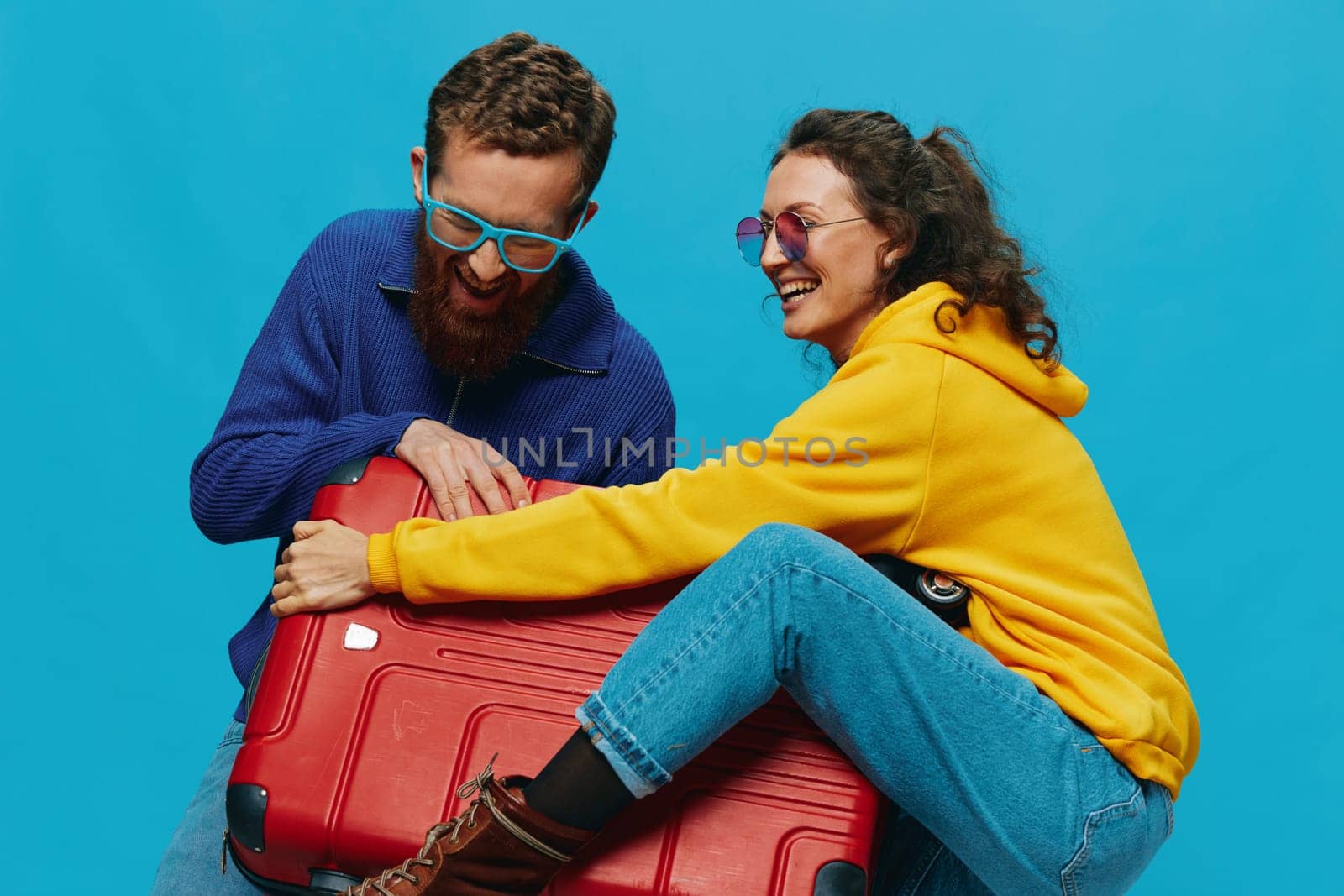 Woman and man smile suitcases in hand with yellow and red suitcase smile fun, on blue background, packing for a trip, family vacation trip. by SHOTPRIME