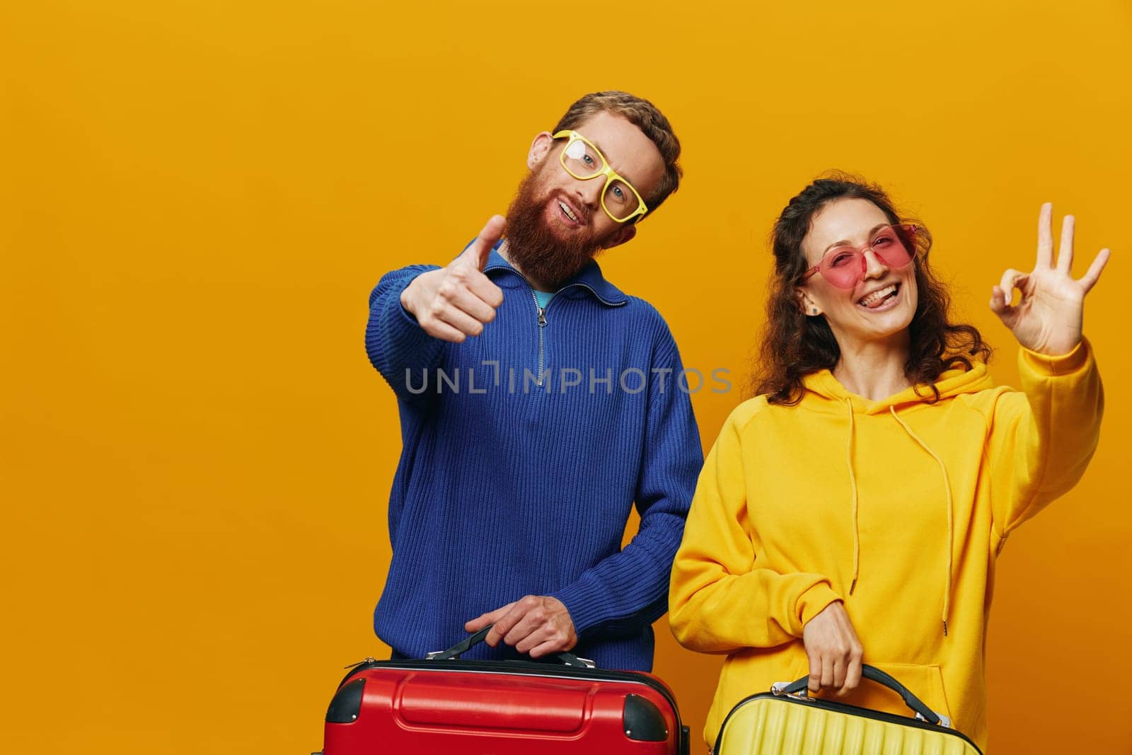 Woman and man smiling, suitcases in hand with yellow and red suitcase smiling merrily and crooked, yellow background, going on a trip, family vacation trip, newlyweds. High quality photo