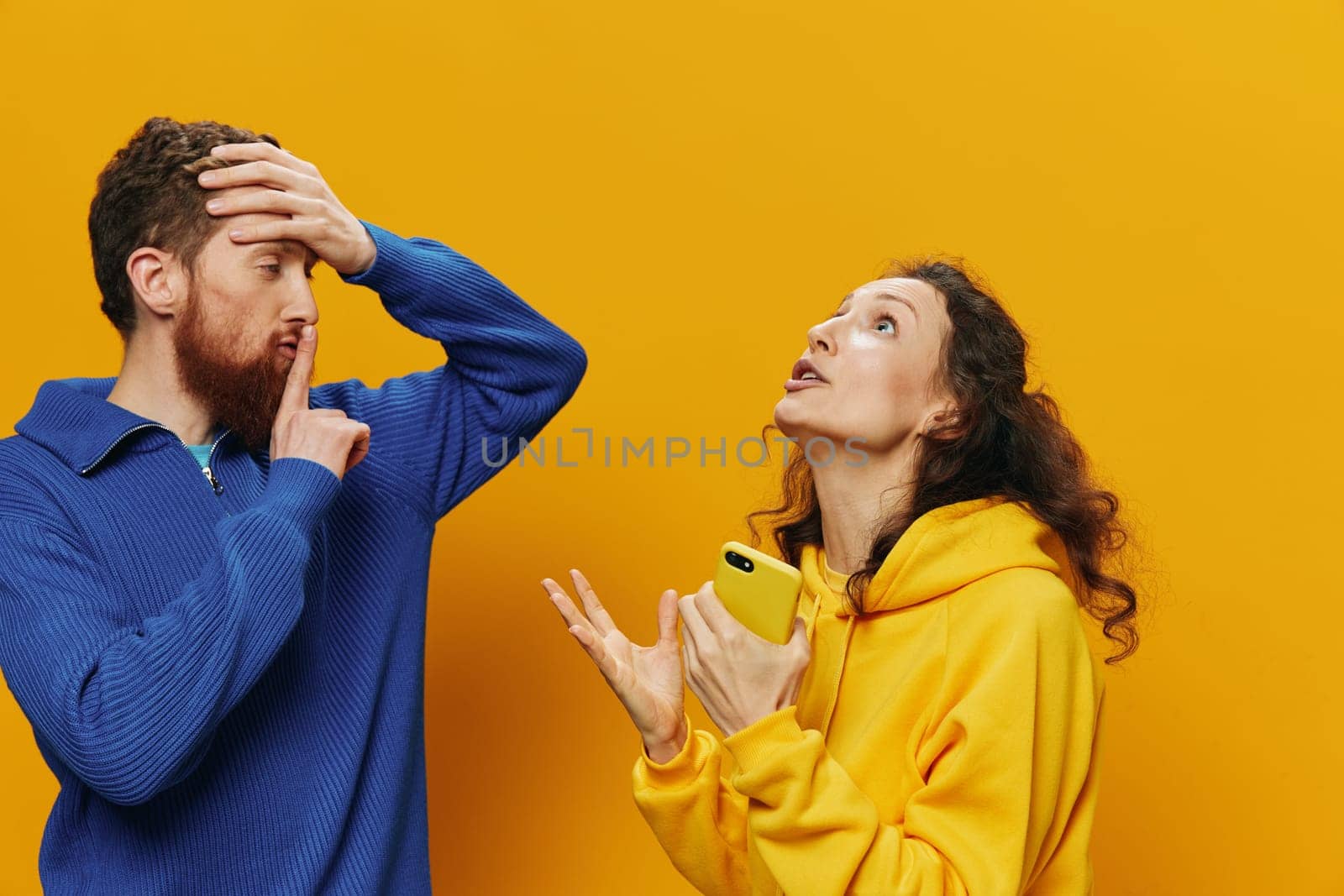 Woman man cheerful couple with phones in hand social networking and communication crooked smile fun and fight, in yellow background. The concept of real family relationships, freelancers, work online. by SHOTPRIME