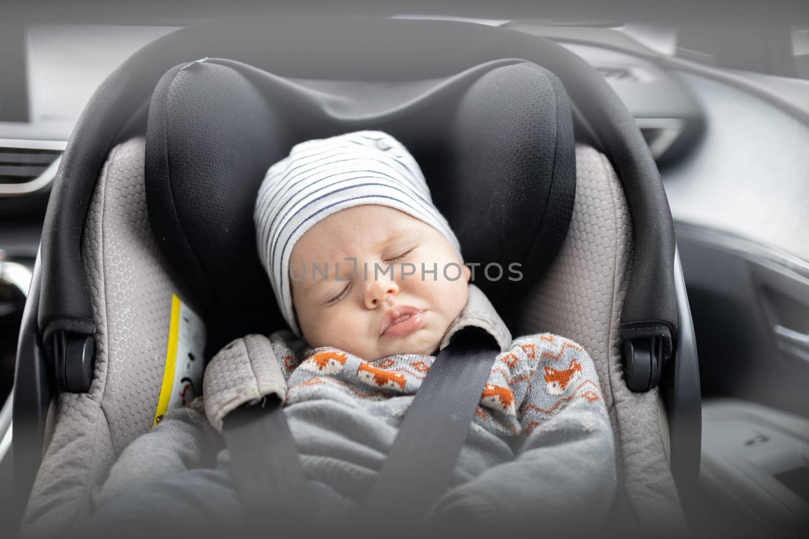 Cute little baby boy sleeping strapped into infant car seat in passenger compartment during car drive