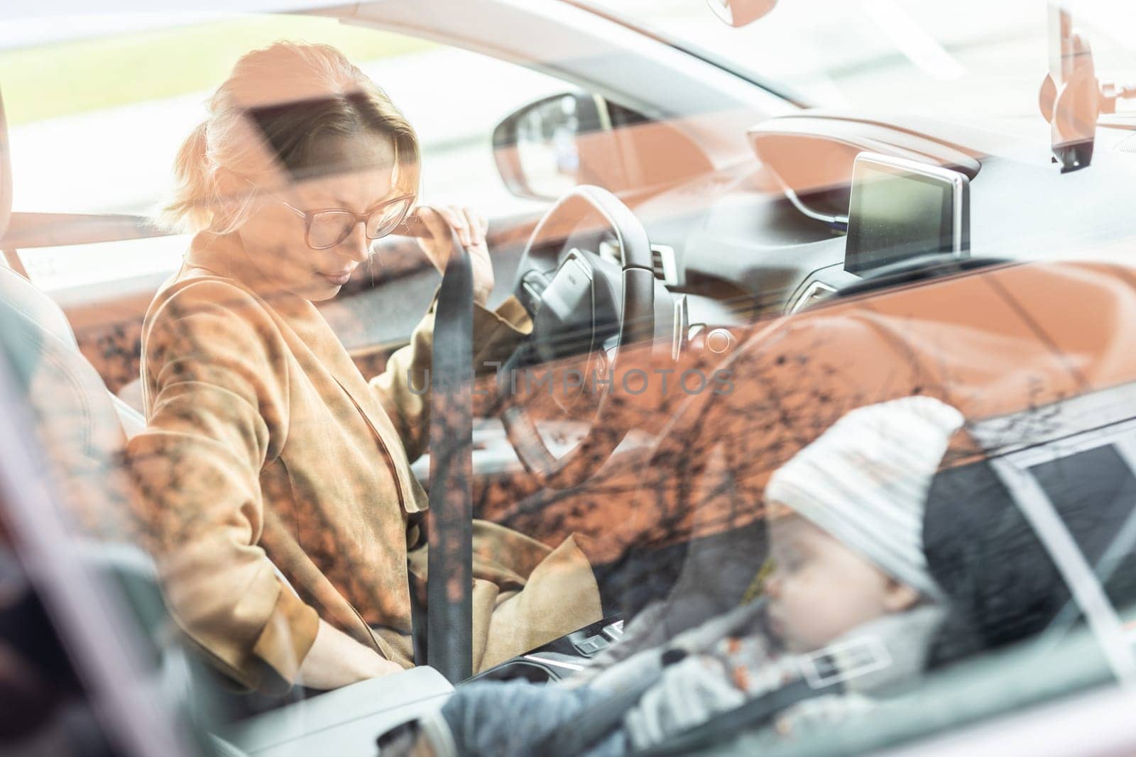 Mother fastening seat belt, driving family car, running errands while her baby sleeps in infant car seat by her site