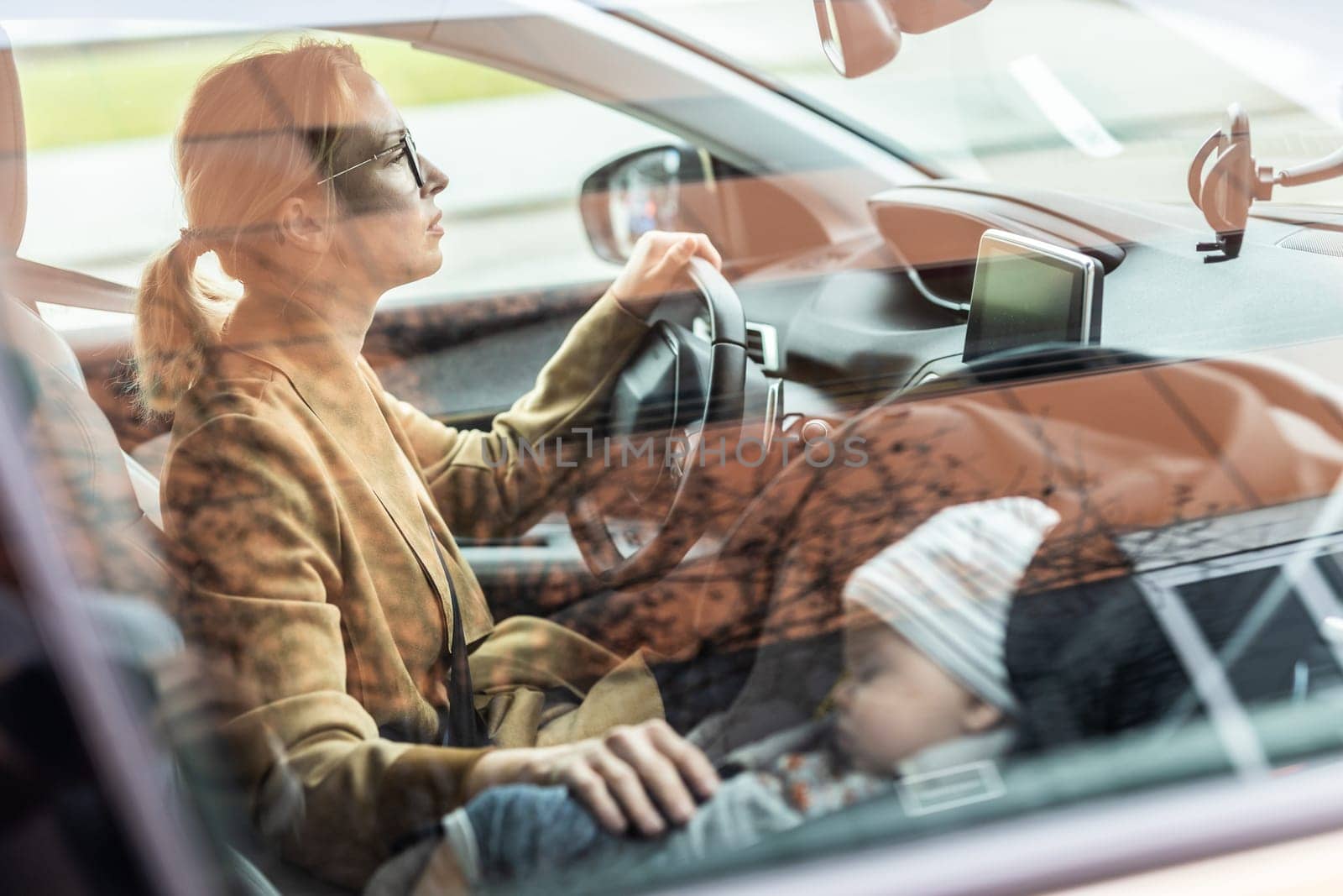 Mother concentrating on driving family car running errands while her baby sleeps in infant car seat by her site. by kasto