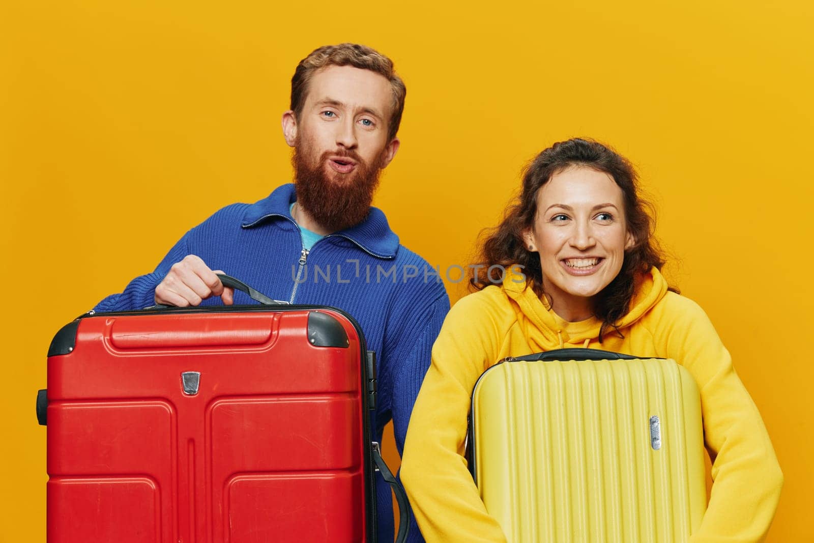 Woman and man smiling, suitcases in hand with yellow and red suitcase smiling merrily and crooked, yellow background, going on a trip, family vacation trip, newlyweds. High quality photo