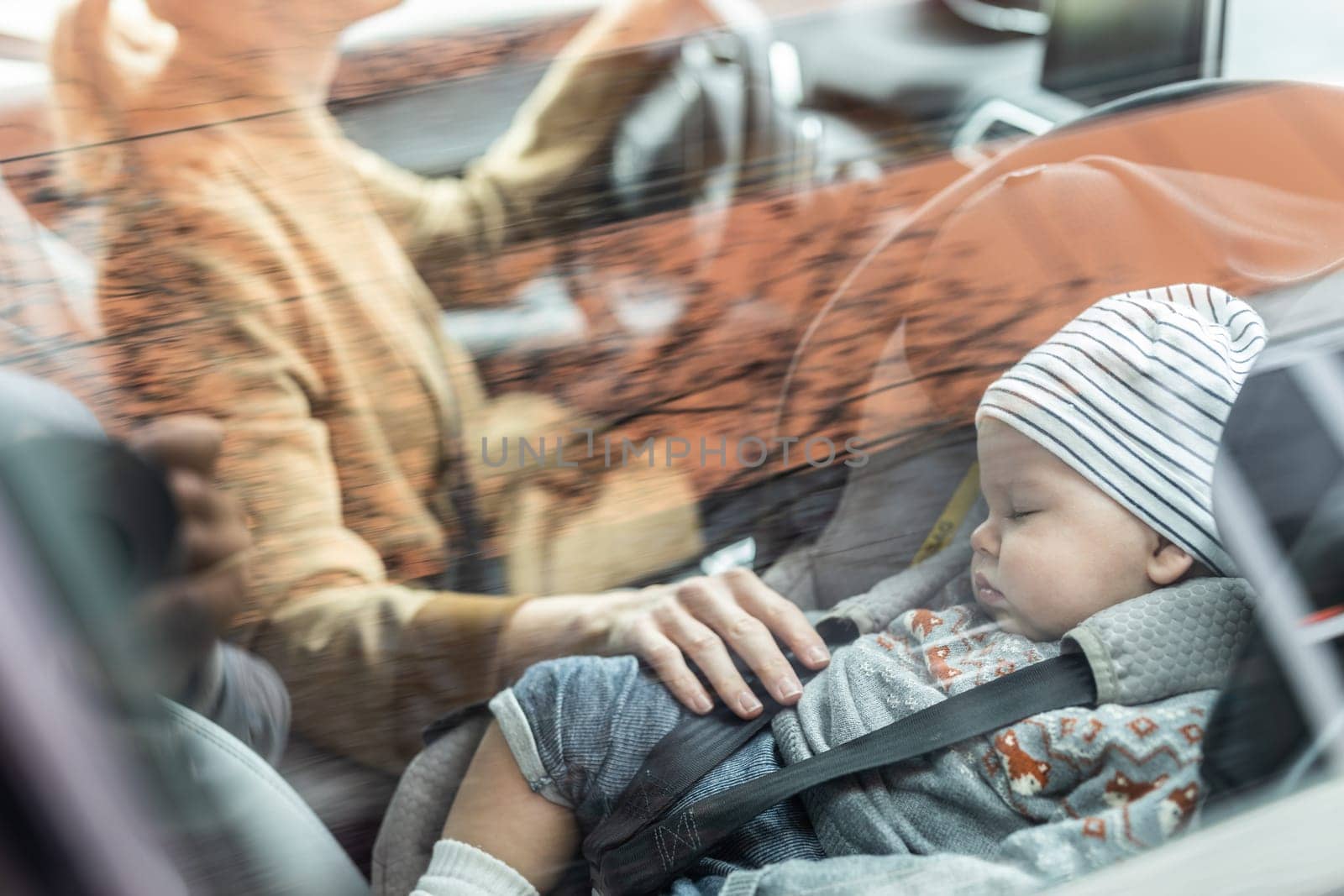 Mother concentrating on driving family car running errands while her baby sleeps in infant car seat by her site. by kasto