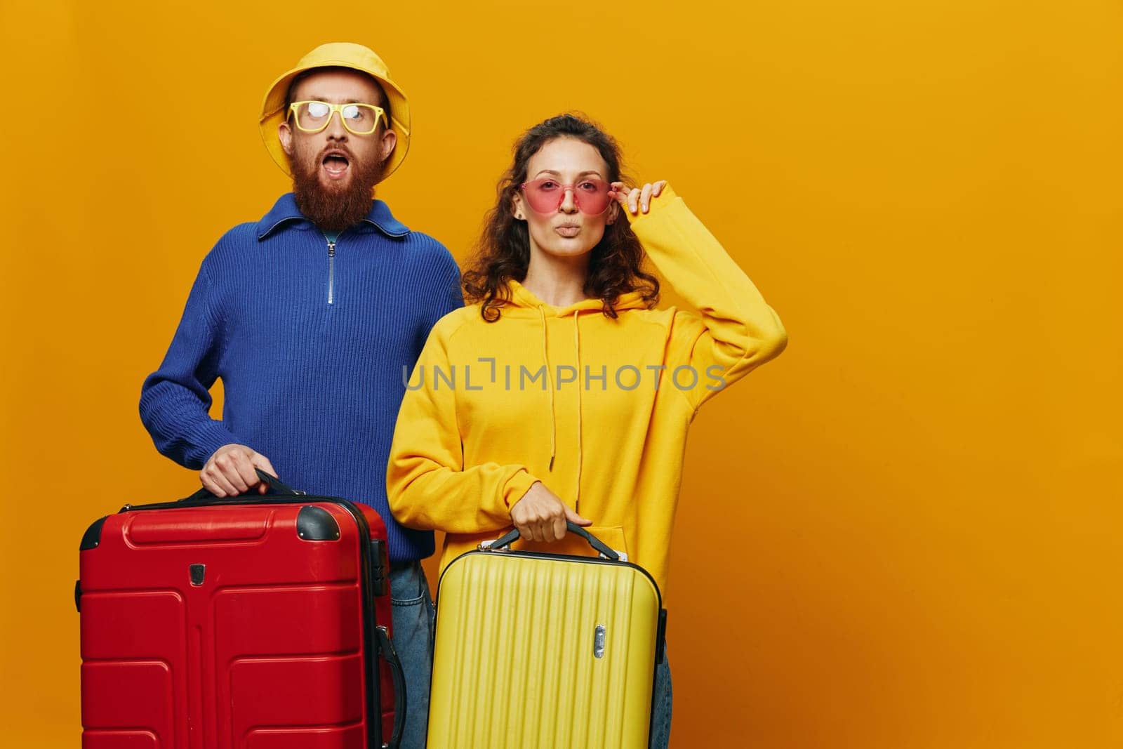 Woman and man smiling, suitcases in hand with yellow and red suitcase smiling merrily and crooked, yellow background, going on a trip, family vacation trip, newlyweds. High quality photo