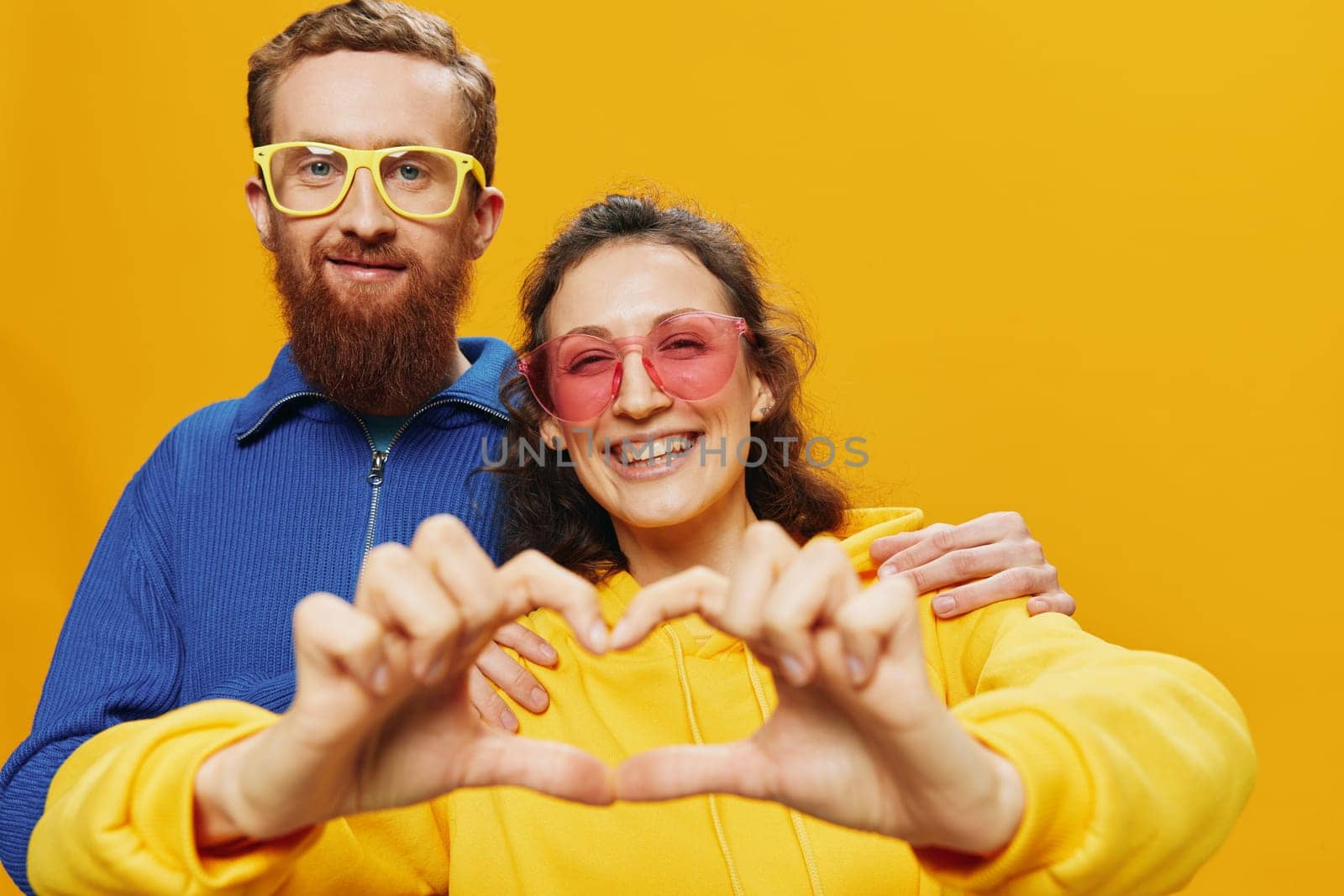 Man and woman couple smiling cheerfully and crooked with glasses, on yellow background, symbols signs and hand gestures, family shoot, newlyweds. High quality photo