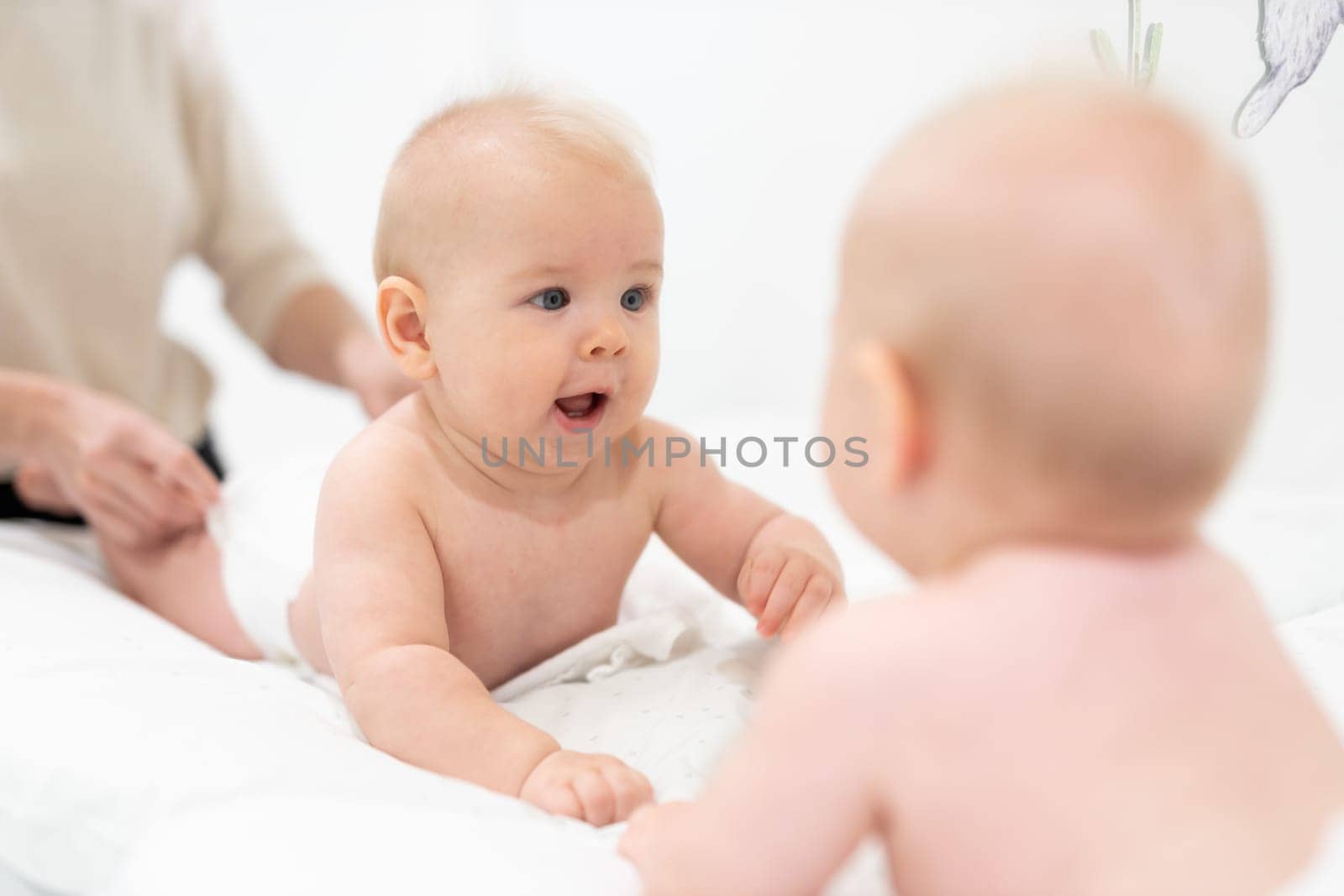 Beautiful shot of a cute baby boy looking at his reflection in big mirror. by kasto