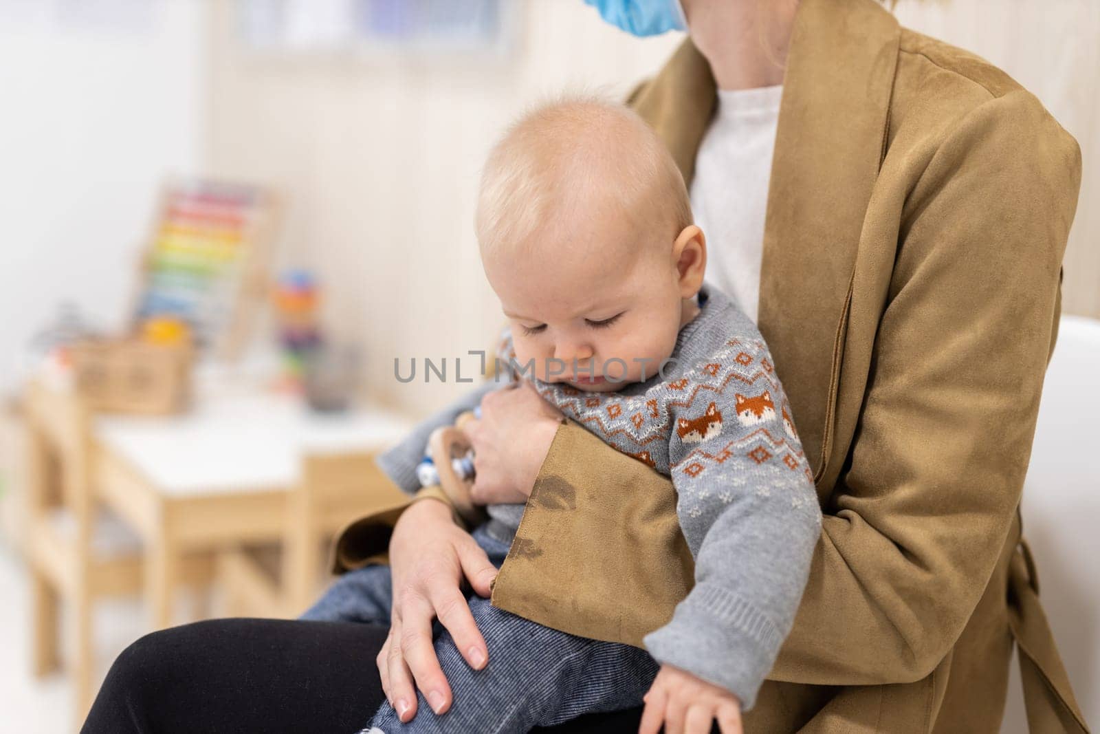 Mother holding infant baby boy in her lap, sitting and waiting in front of doctor's office for pediatric well check. child's health care concept by kasto