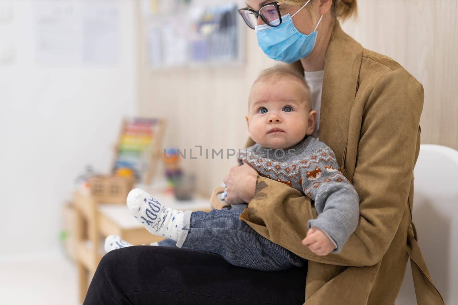 Mother holding infant baby boy in her lap, sitting and waiting in front of doctor's office for pediatric well check. child's health care concept by kasto
