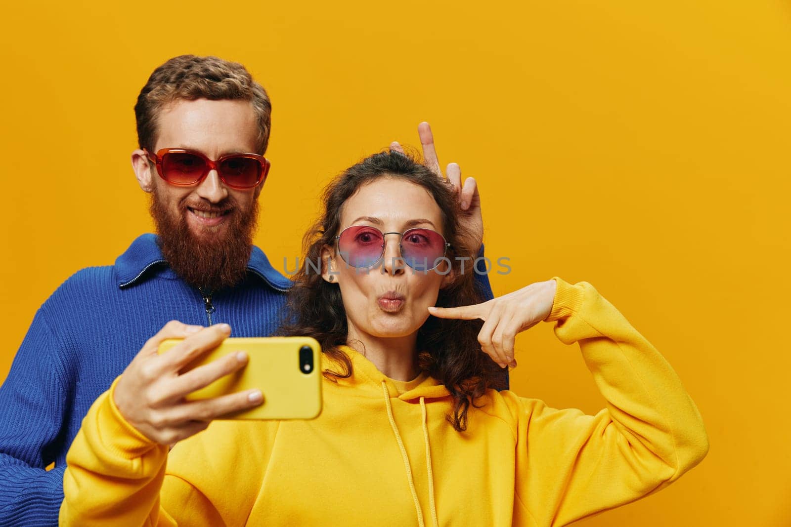 Woman and man funny couple with phones in hand social networking and communication crooked do selfies smile fun, on yellow background. The concept of real family relationships, freelancers, work online. High quality photo