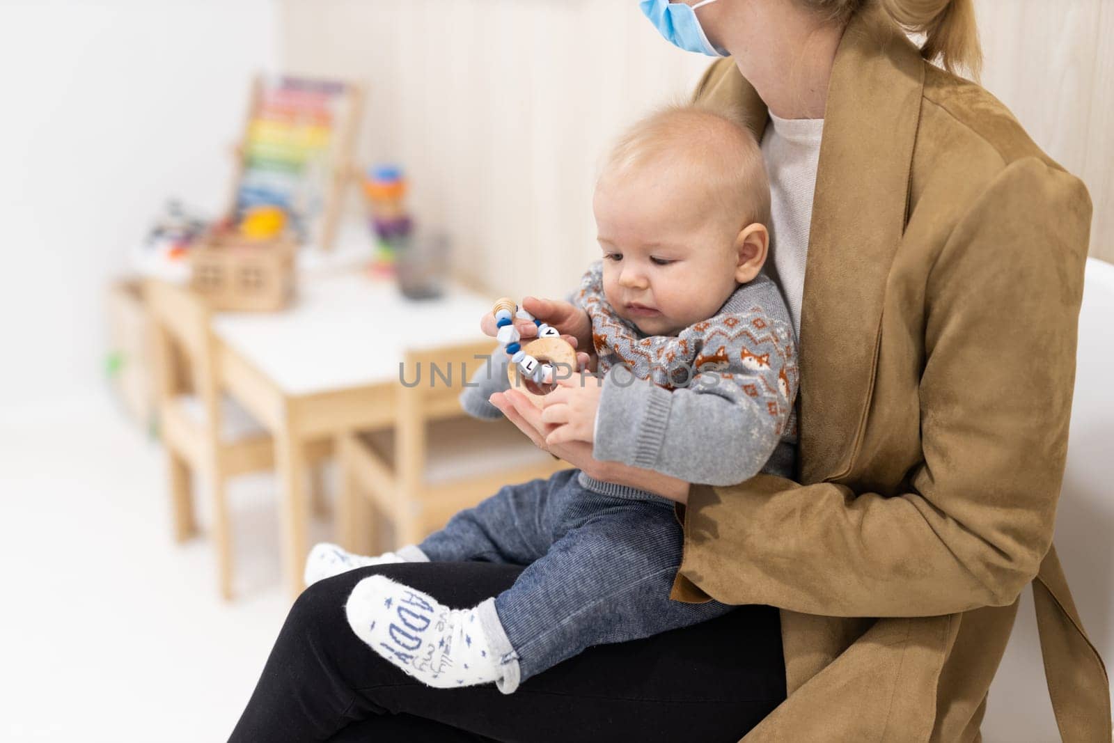 Mother holding infant baby boy in her lap, sitting and waiting in front of doctor's office for pediatric well check. child's health care concept.