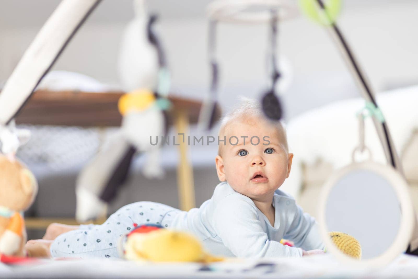 Cute baby boy playing with hanging toys arch on mat at home Baby activity and play center for early infant development. Baby playing at home.