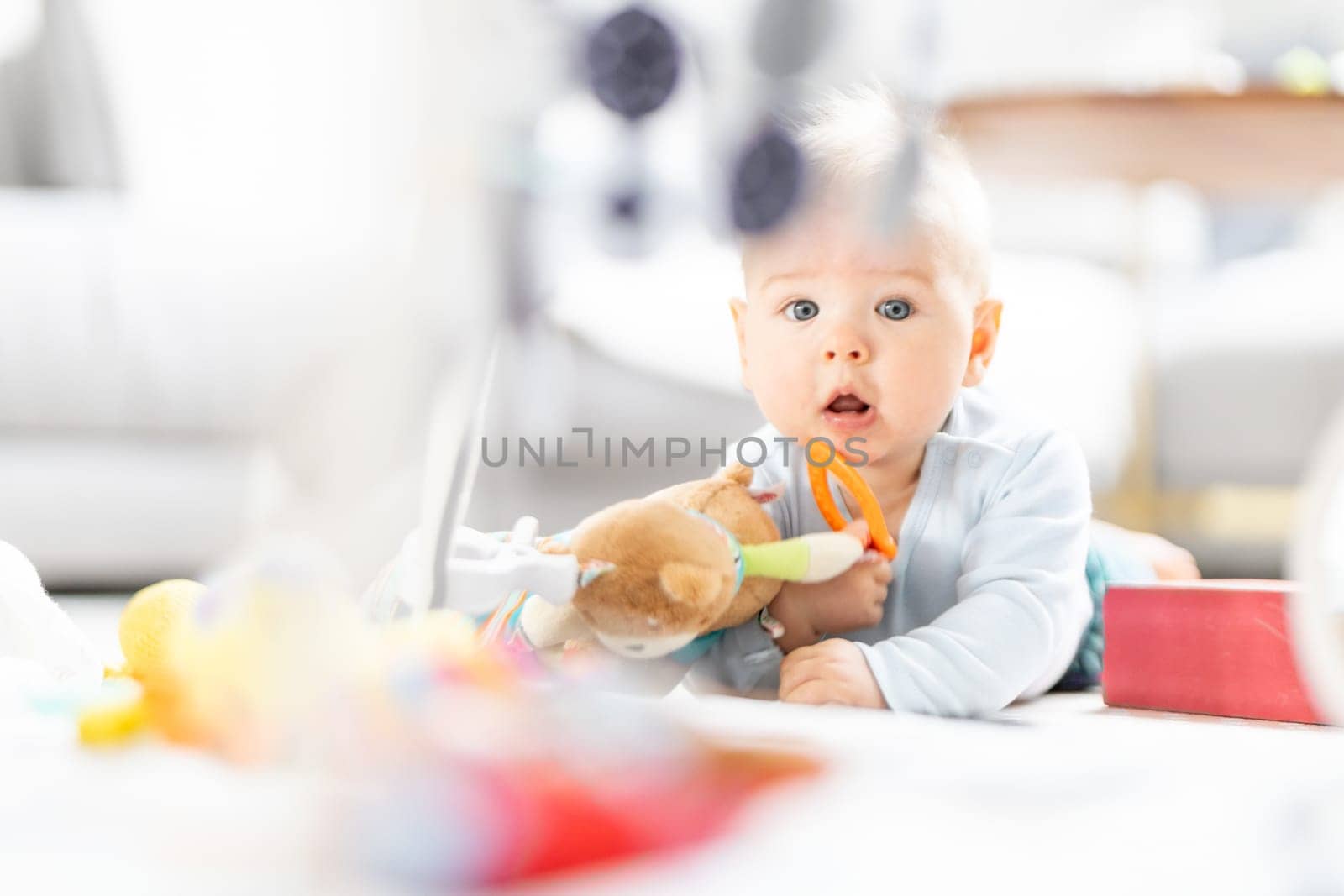 Cute baby boy playing with hanging toys arch on mat at home Baby activity and play center for early infant development. Baby playing at home.