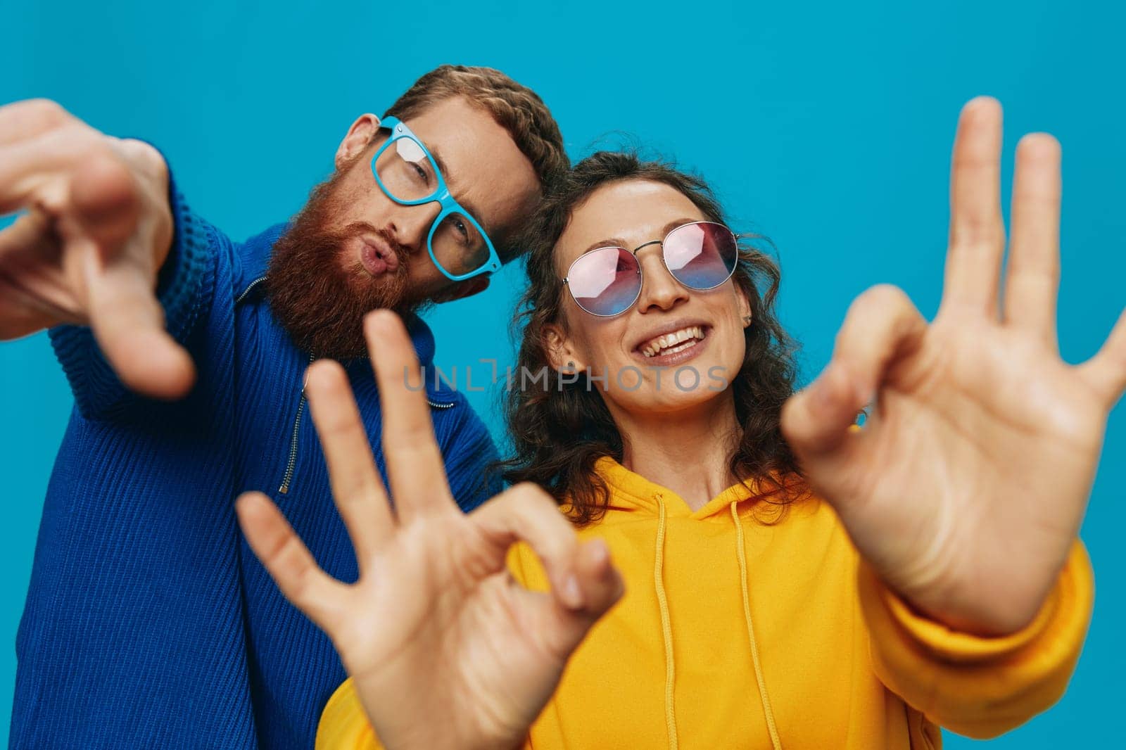 A woman and a man fun couple cranking and showing signs with their hands smiling cheerfully, on a blue background, The concept of a real relationship in a family. High quality photo