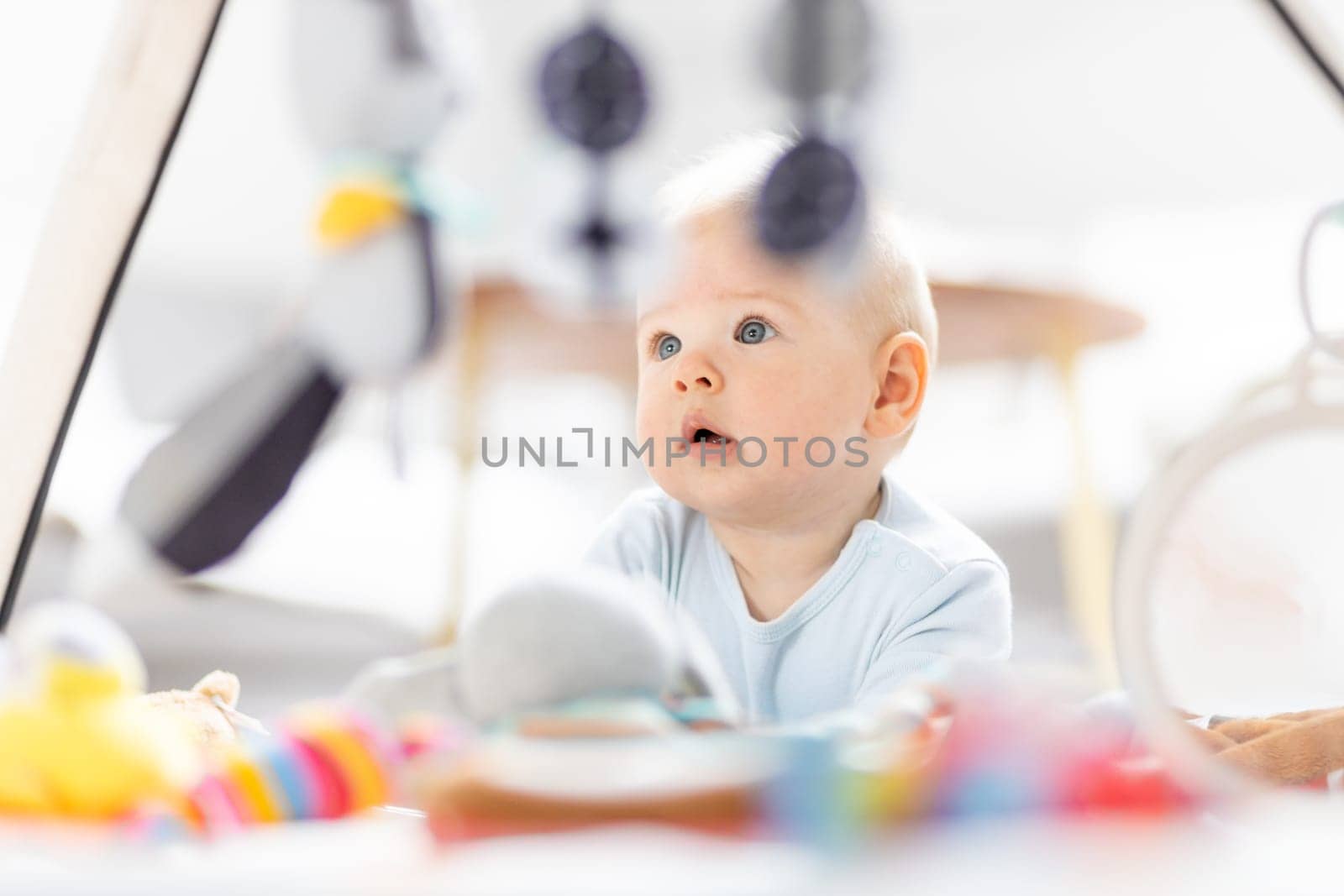 Cute baby boy playing with hanging toys arch on mat at home Baby activity and play center for early infant development. Baby playing at home.