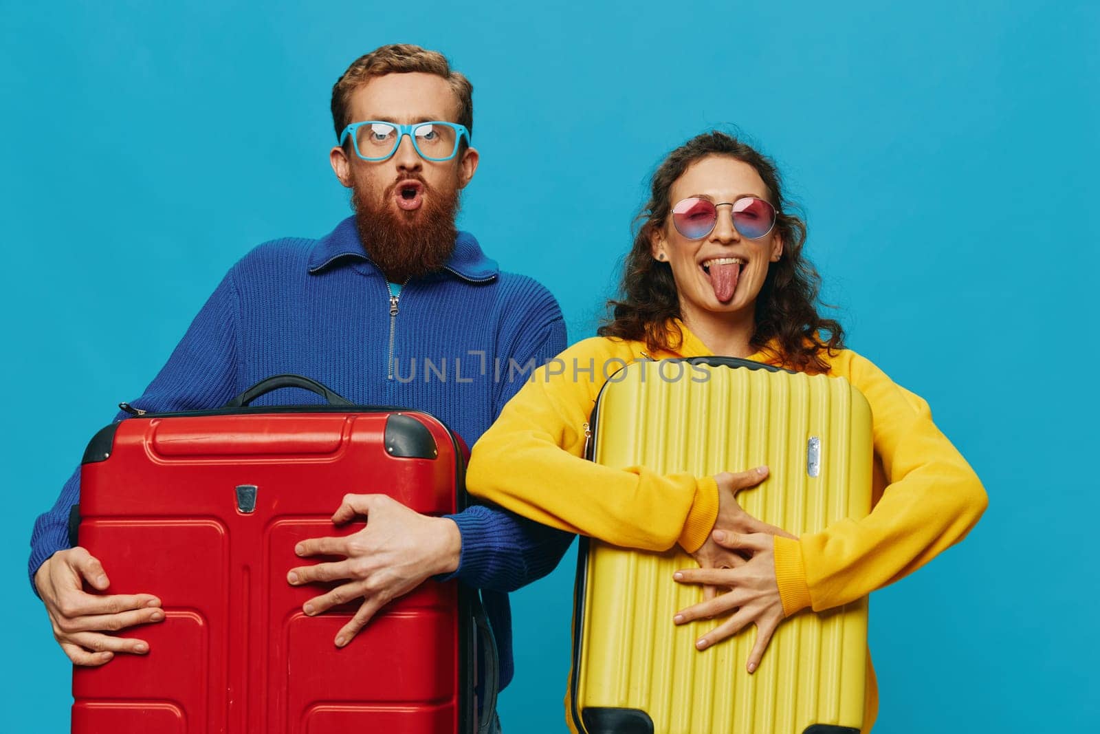 Woman and man smile suitcases in hand with yellow and red suitcase smile fun, on blue background, packing for a trip, family vacation trip. High quality photo