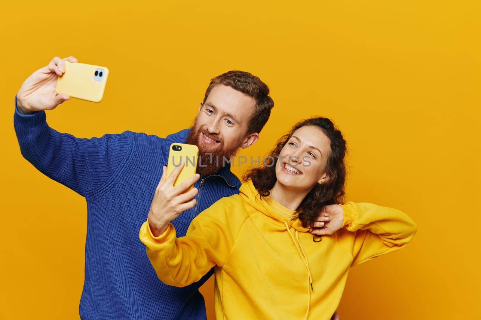 Man and woman couple smiling merrily with phone in hand social media viewing photos and videos, on yellow background, symbols signs and hand gestures, family freelancers. High quality photo