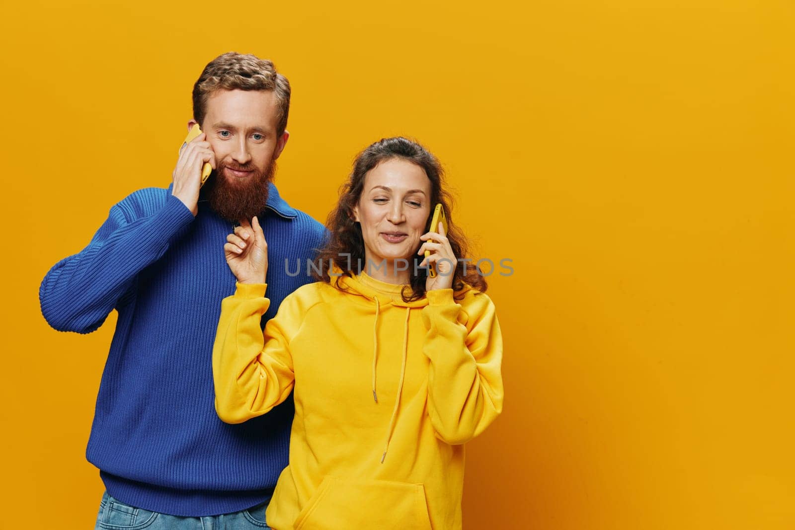 Man and woman couple smiling merrily with phone in hand social media viewing photos and videos, on yellow background, symbols signs and hand gestures, family freelancers. High quality photo