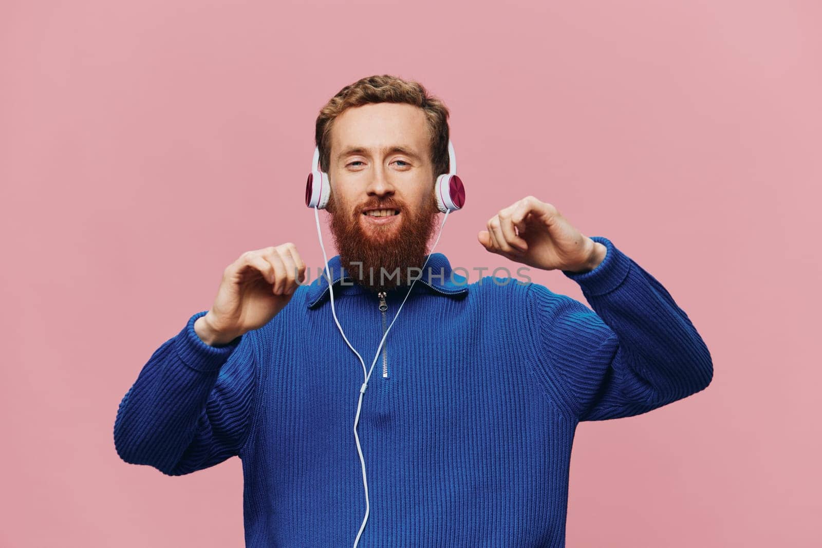 Portrait of a redheaded man wearing headphones smiling and dancing, listening to music on a pink background. A hipster with a beard. by SHOTPRIME