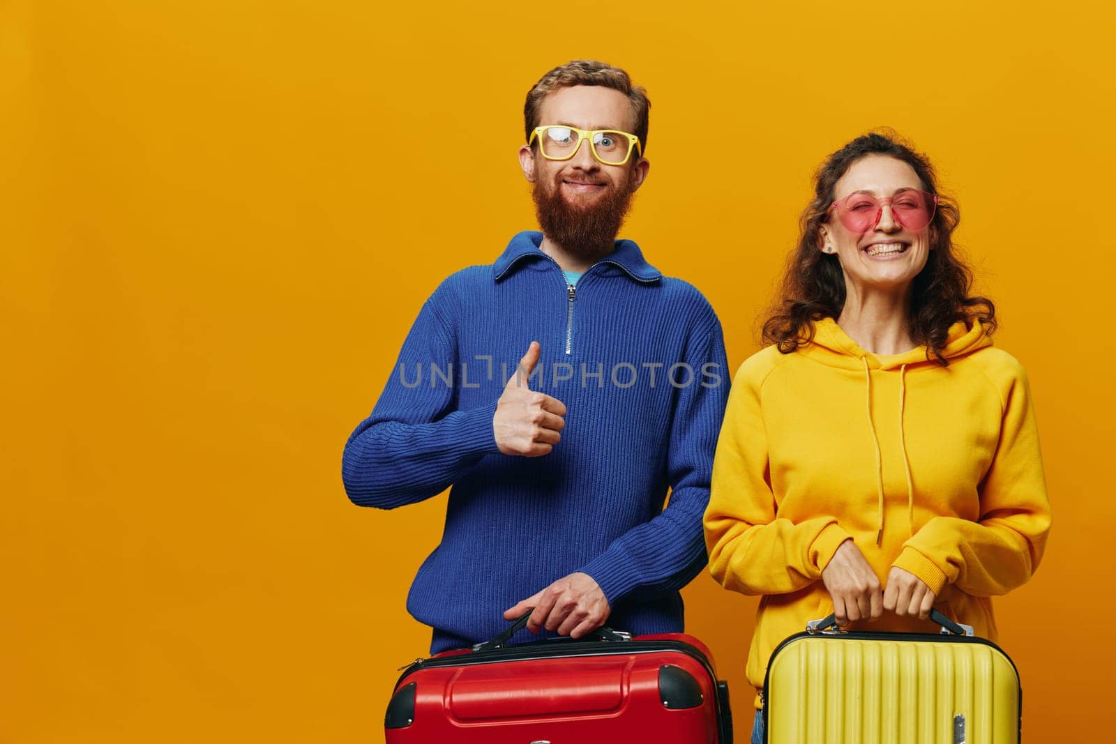 Woman and man smiling, suitcases in hand with yellow and red suitcase smiling merrily and crooked, yellow background, going on a trip, family vacation trip, newlyweds. High quality photo