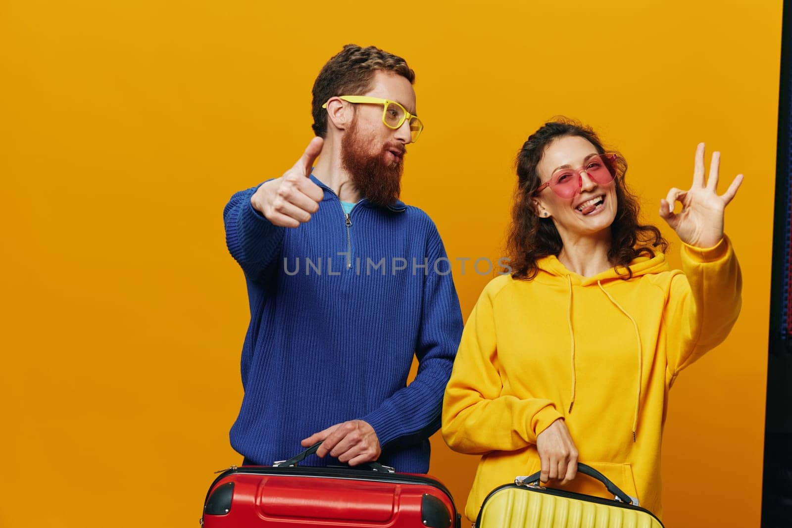 Woman and man smiling, suitcases in hand with yellow and red suitcase smiling merrily and crooked, yellow background, going on a trip, family vacation trip, newlyweds. High quality photo