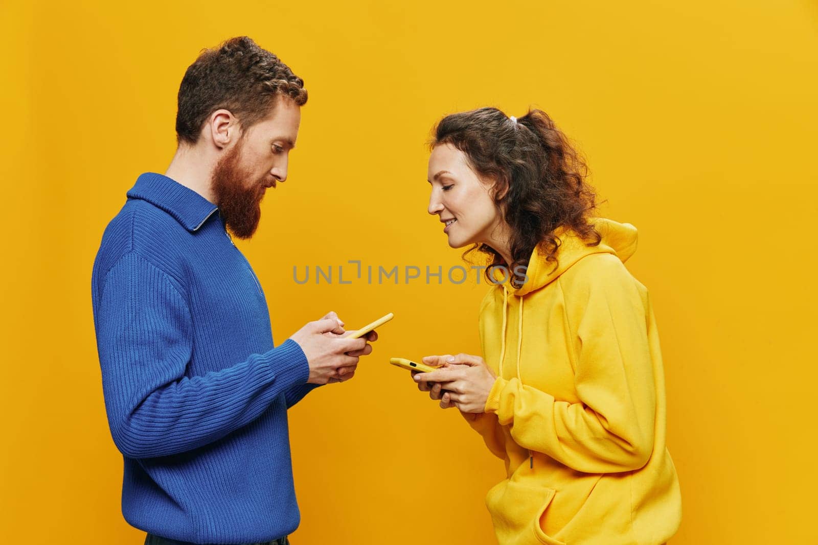 Woman and man cheerful couple with phones in hand social networking and communication crooked smile fun and fight, in yellow background. The concept of real family relationships, freelancers, work online. High quality photo