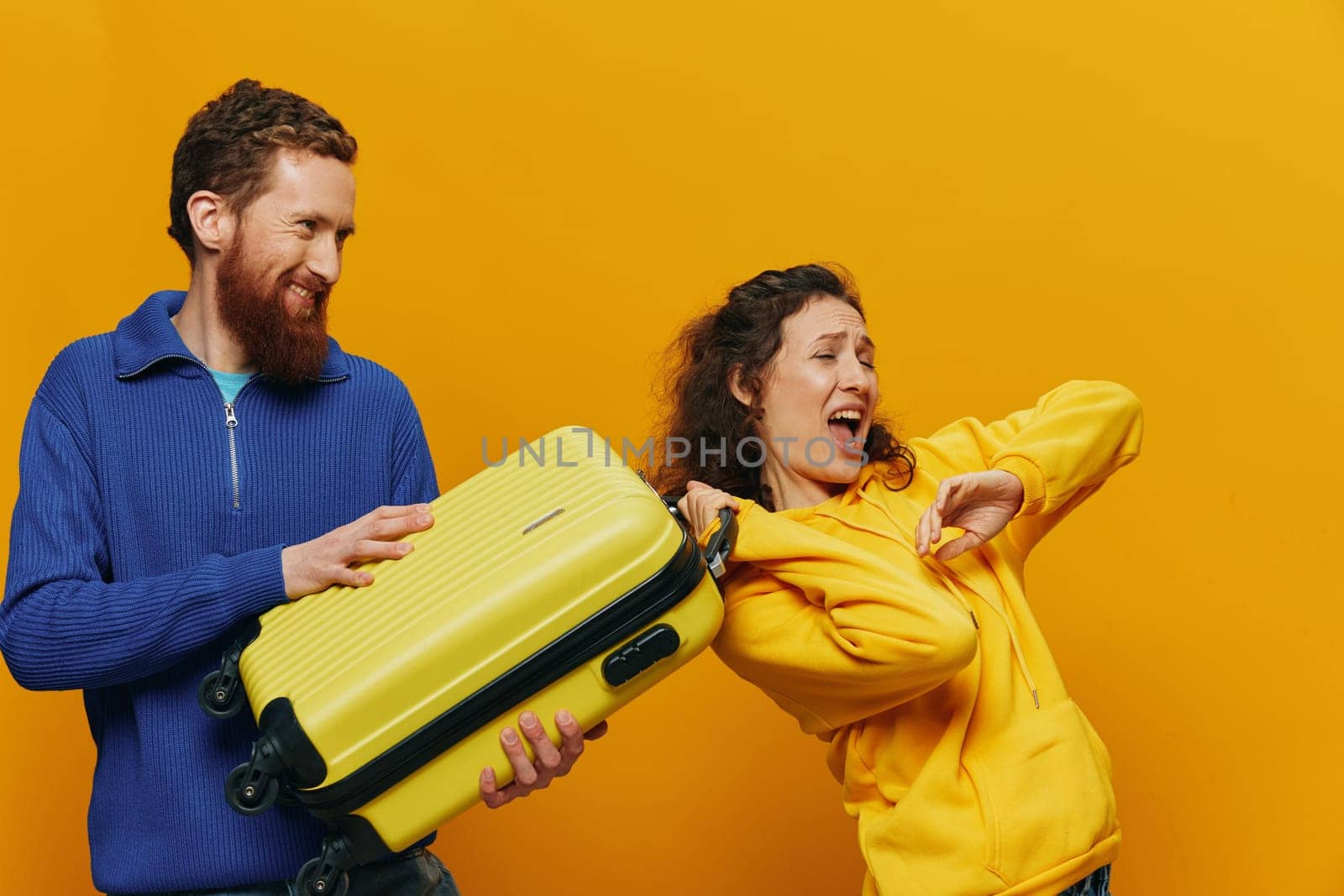 Woman and man smiling, suitcases in hand with yellow and red suitcase smiling merrily and crooked, yellow background, going on a trip, family vacation trip, newlyweds. High quality photo