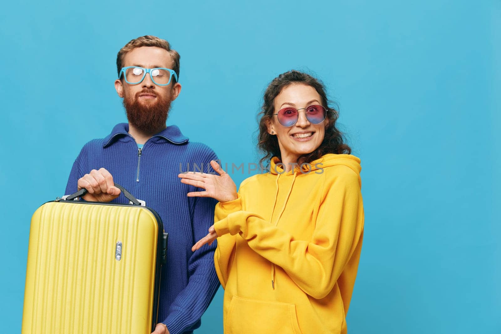 Woman and man smile sitting on suitcase with yellow suitcase smile, on blue background, packing for trip, family vacation trip. High quality photo