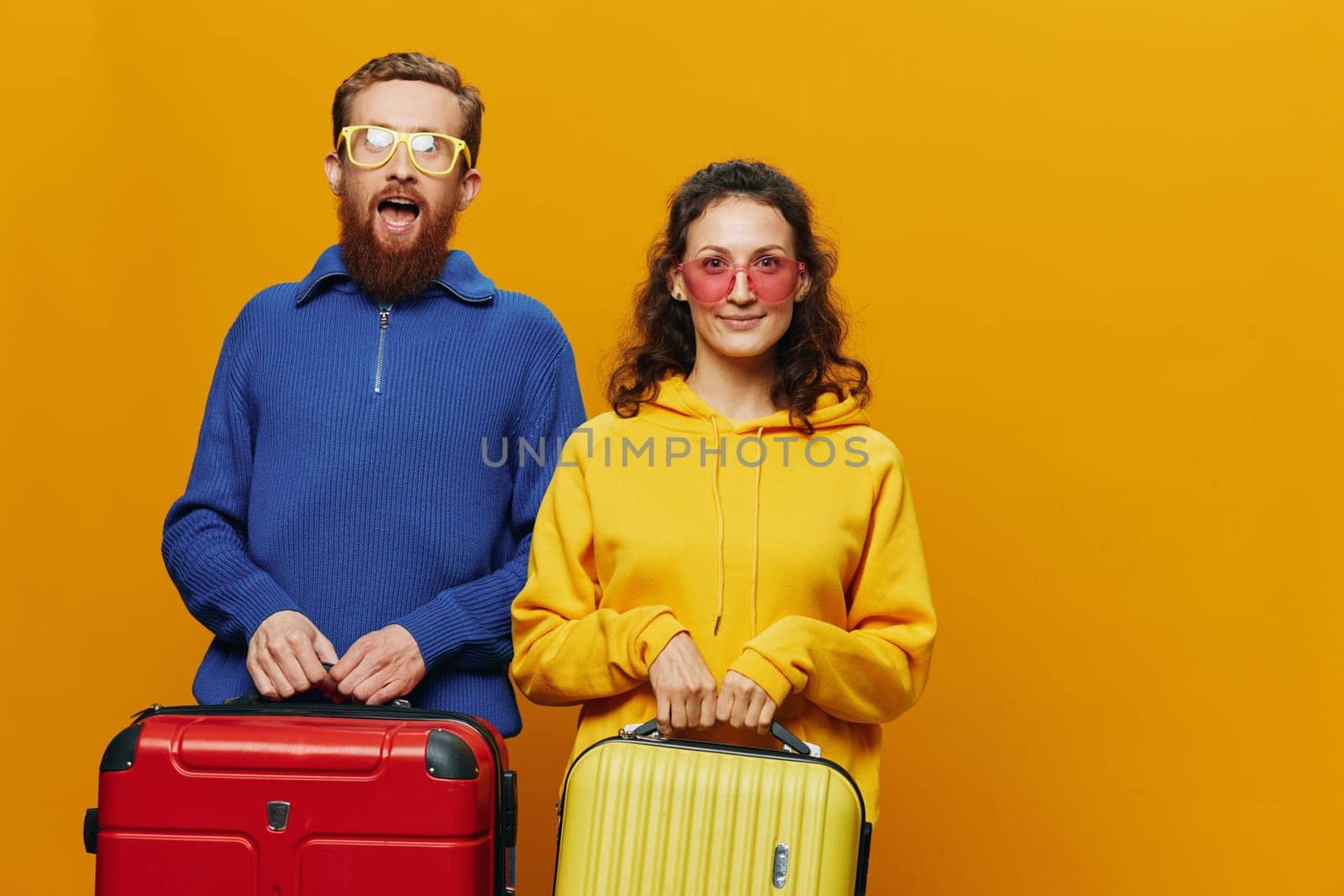 Woman and man smiling, suitcases in hand with yellow and red suitcase smiling merrily and crooked, yellow background, going on a trip, family vacation trip, newlyweds. High quality photo