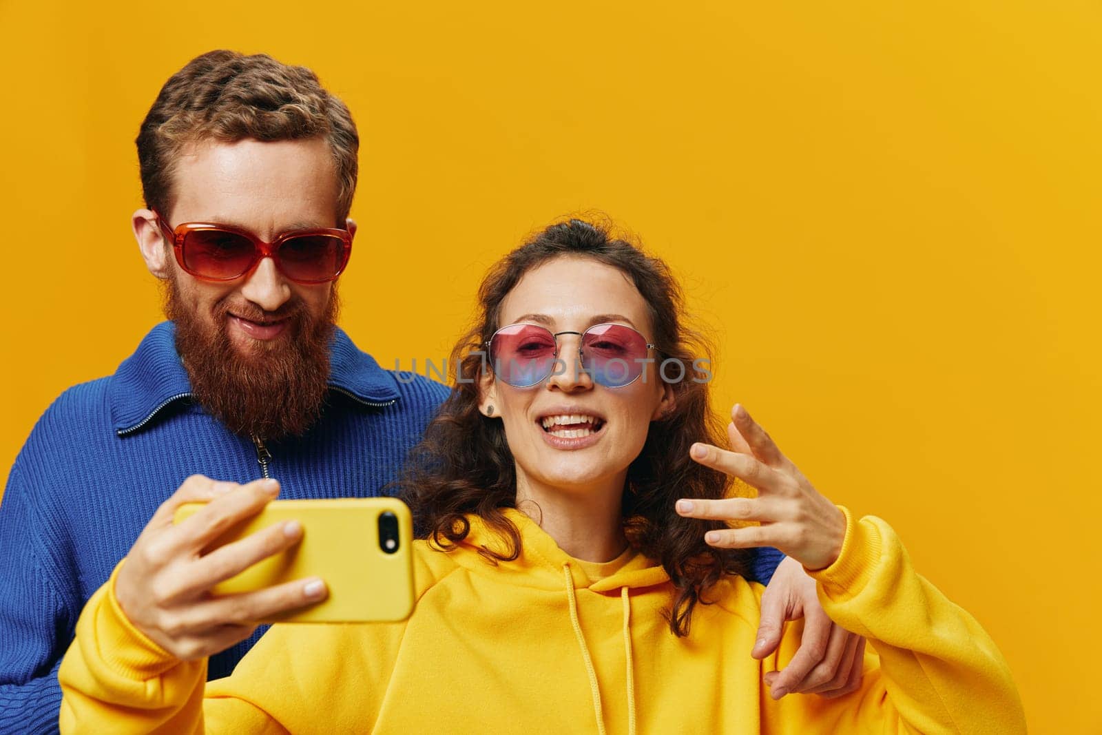 Woman and man funny couple with phones in hand social networking and communication crooked do selfies smile fun, on yellow background. The concept of real family relationships, freelancers, work online. High quality photo