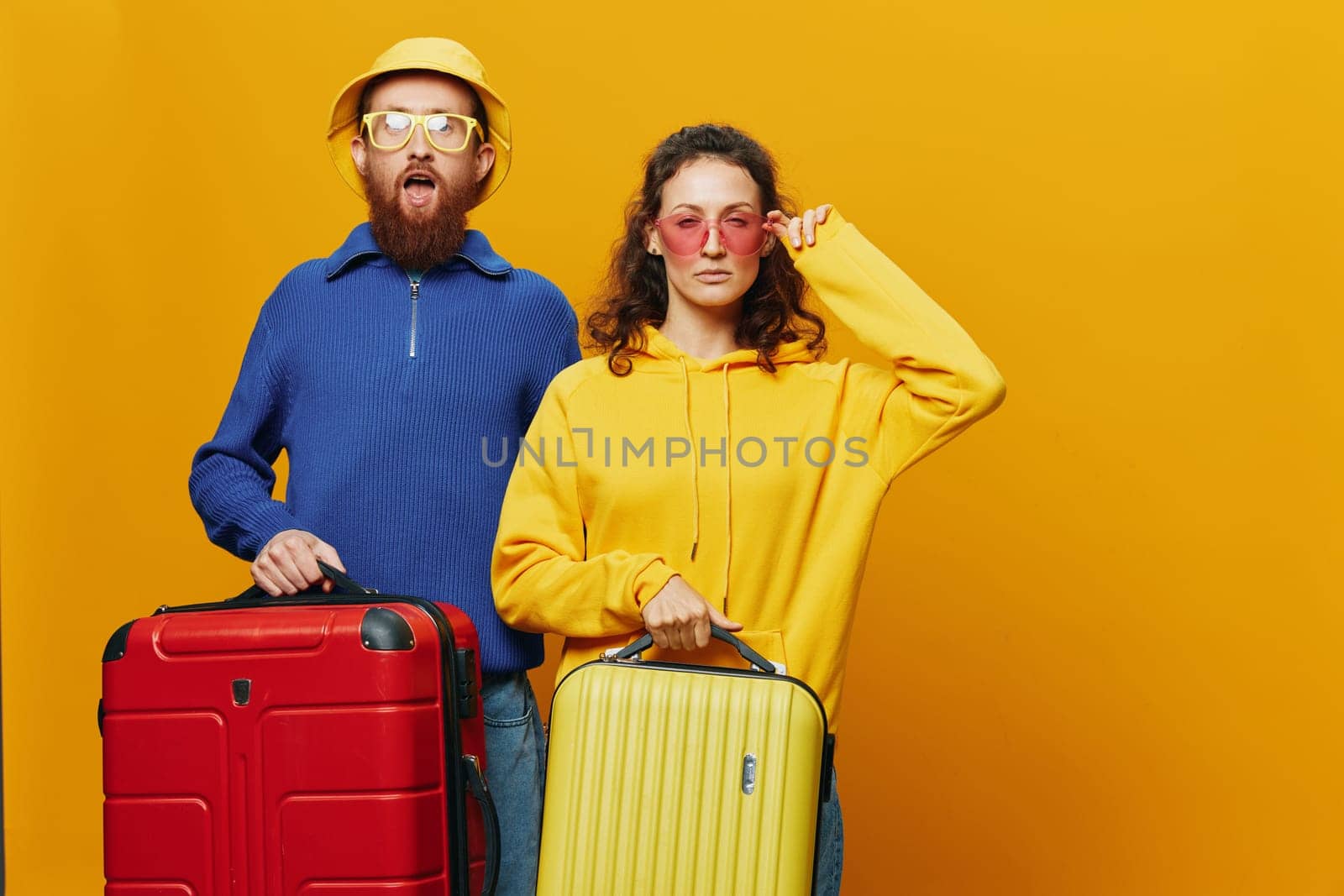 Woman and man smiling, suitcases in hand with yellow and red suitcase smiling merrily and crooked, yellow background, going on a trip, family vacation trip, newlyweds. High quality photo