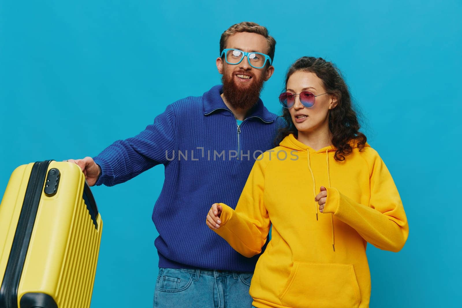 Woman and man smile sitting on suitcase with yellow suitcase smile, on blue background, packing for trip, family vacation trip. High quality photo