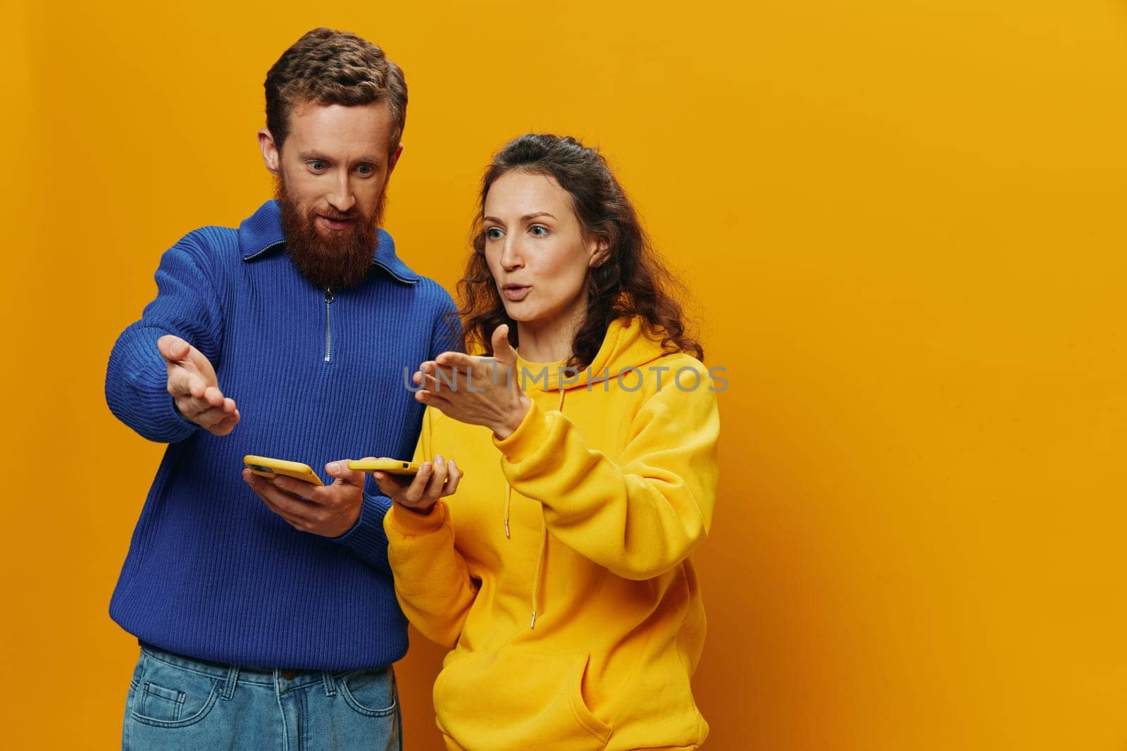 Woman and man cheerful couple with phones in hand social networking and communication crooked smile fun and fight, in yellow background. The concept of real family relationships, freelancers, work online. High quality photo