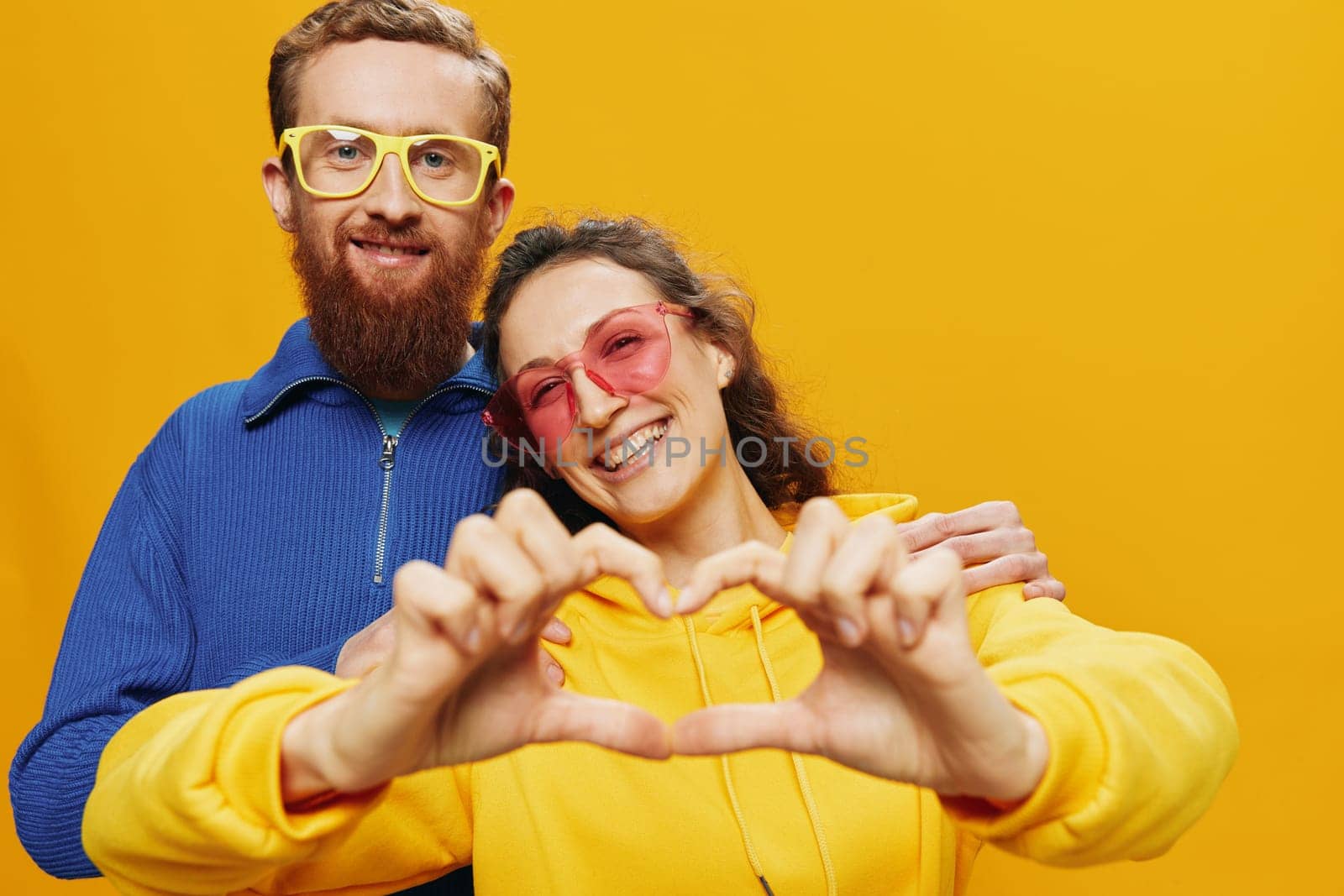 Man and woman couple smiling cheerfully and crooked with glasses, on yellow background, symbols signs and hand gestures, family shoot, newlyweds. High quality photo