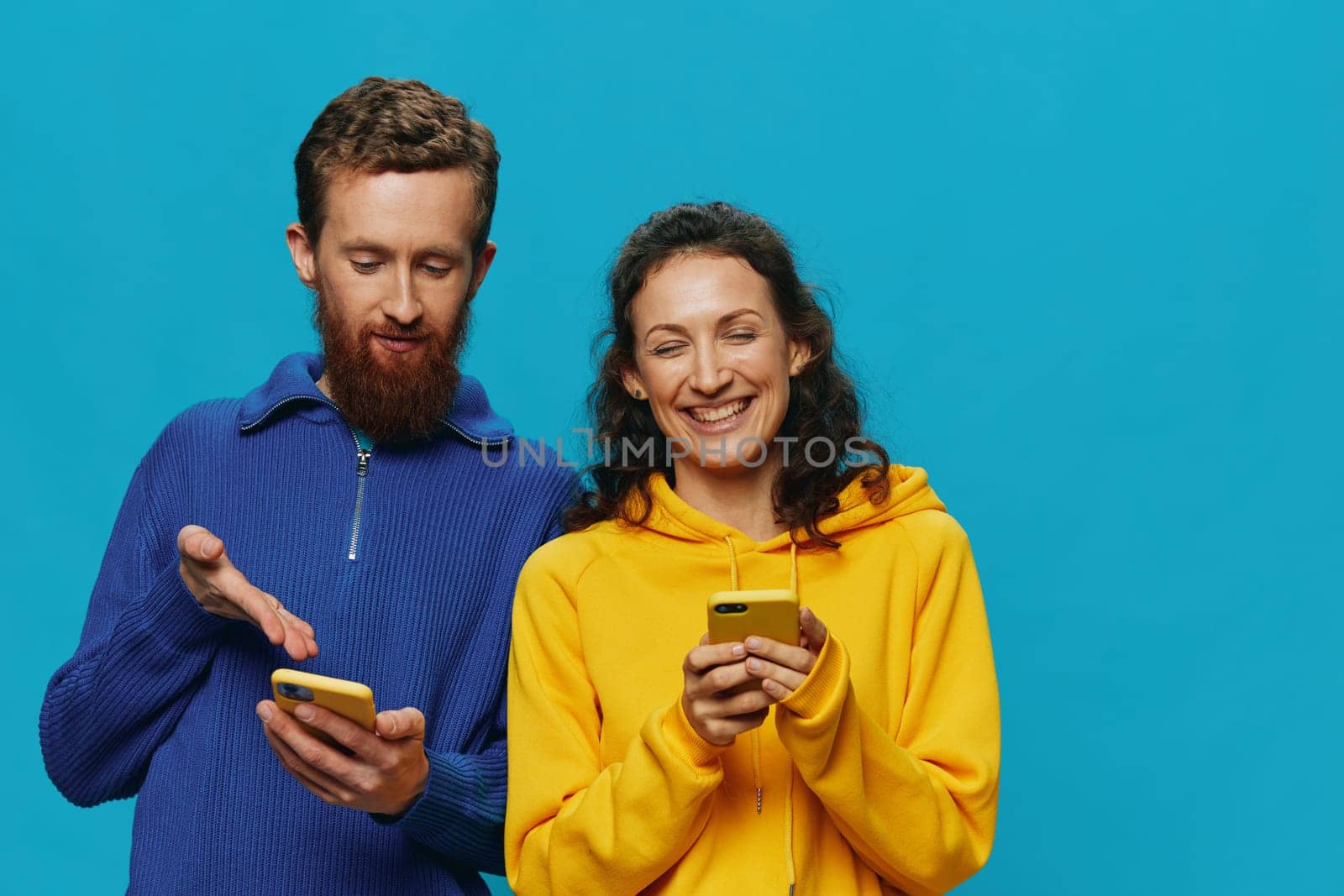 Woman and man cheerful couple with phones in their hands crooked smile cheerful, on blue background. The concept of real family relationships, talking on the phone, work online. High quality photo