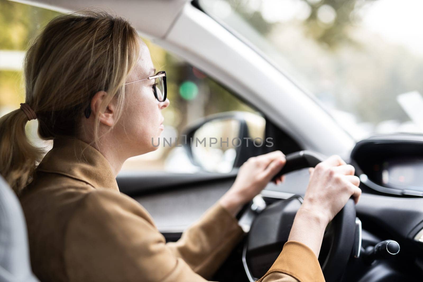 Business woman driving a car to work. Female driver steering car on the road.