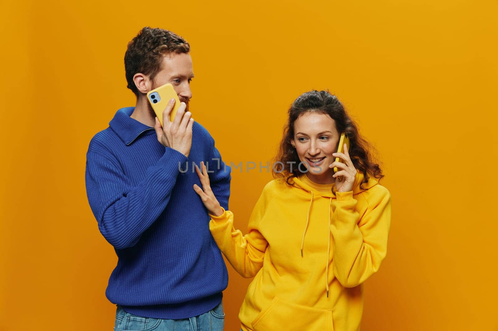 Woman and man cheerful couple with phones in hand talking on cell phone crooked smile cheerful, on yellow background. The concept of real family relationships, talking on the phone, work online. High quality photo