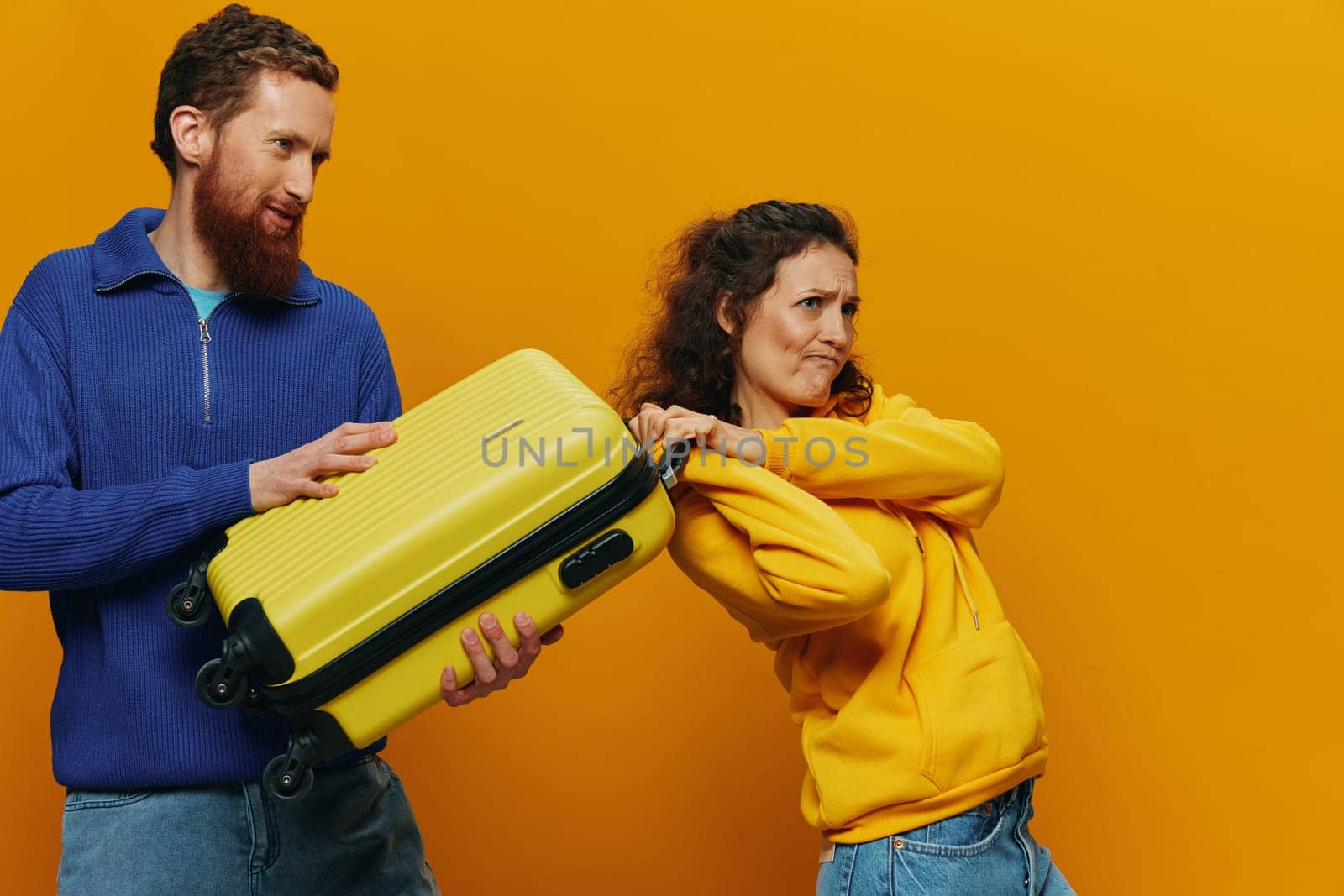 Woman and man smiling, suitcases in hand with yellow and red suitcase smiling merrily and crooked, yellow background, going on a trip, family vacation trip, newlyweds. by SHOTPRIME