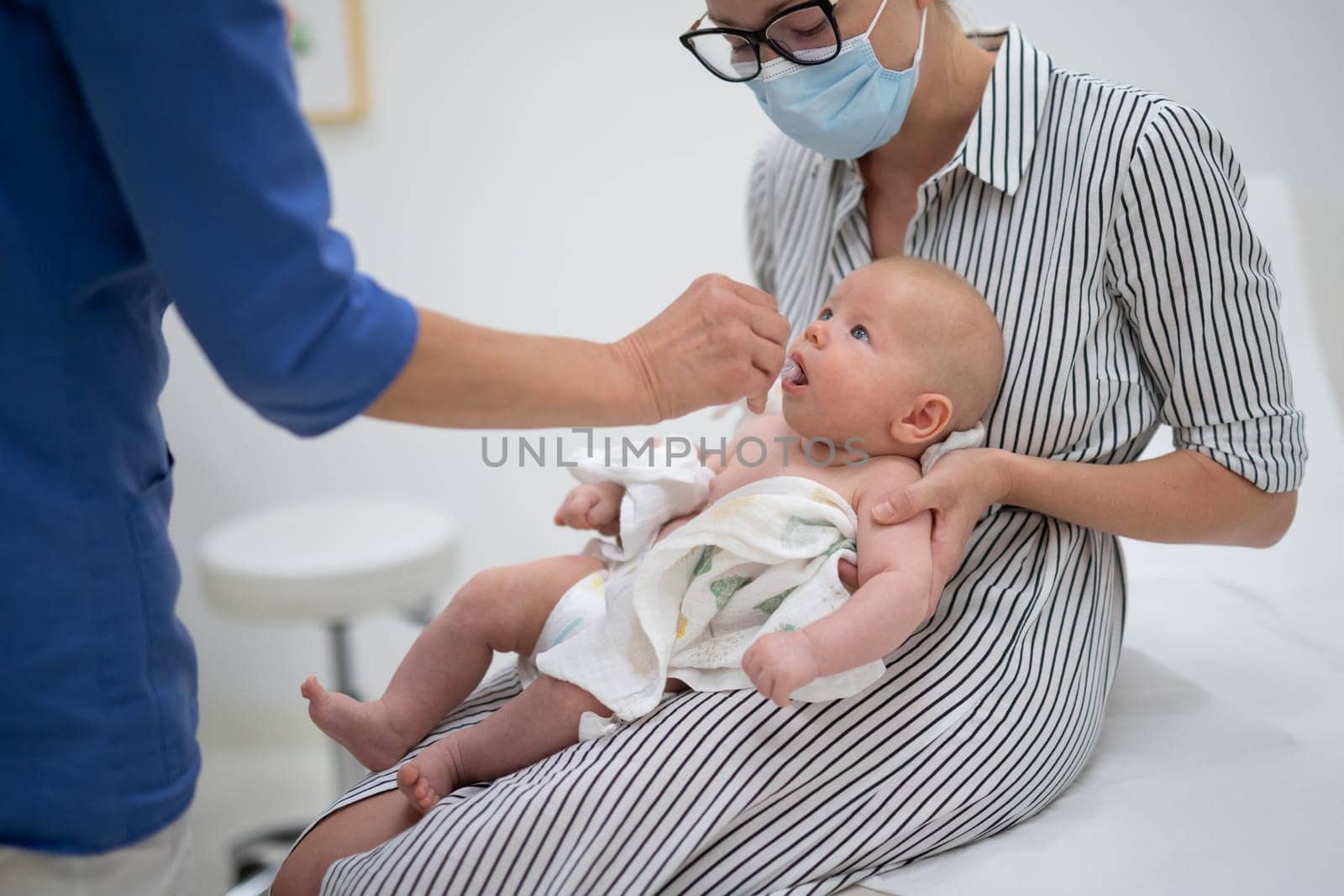 Pediatrician administring oral vaccination against rotavirus infection to little baby in presence of his mother. Children health care and disease prevention by kasto