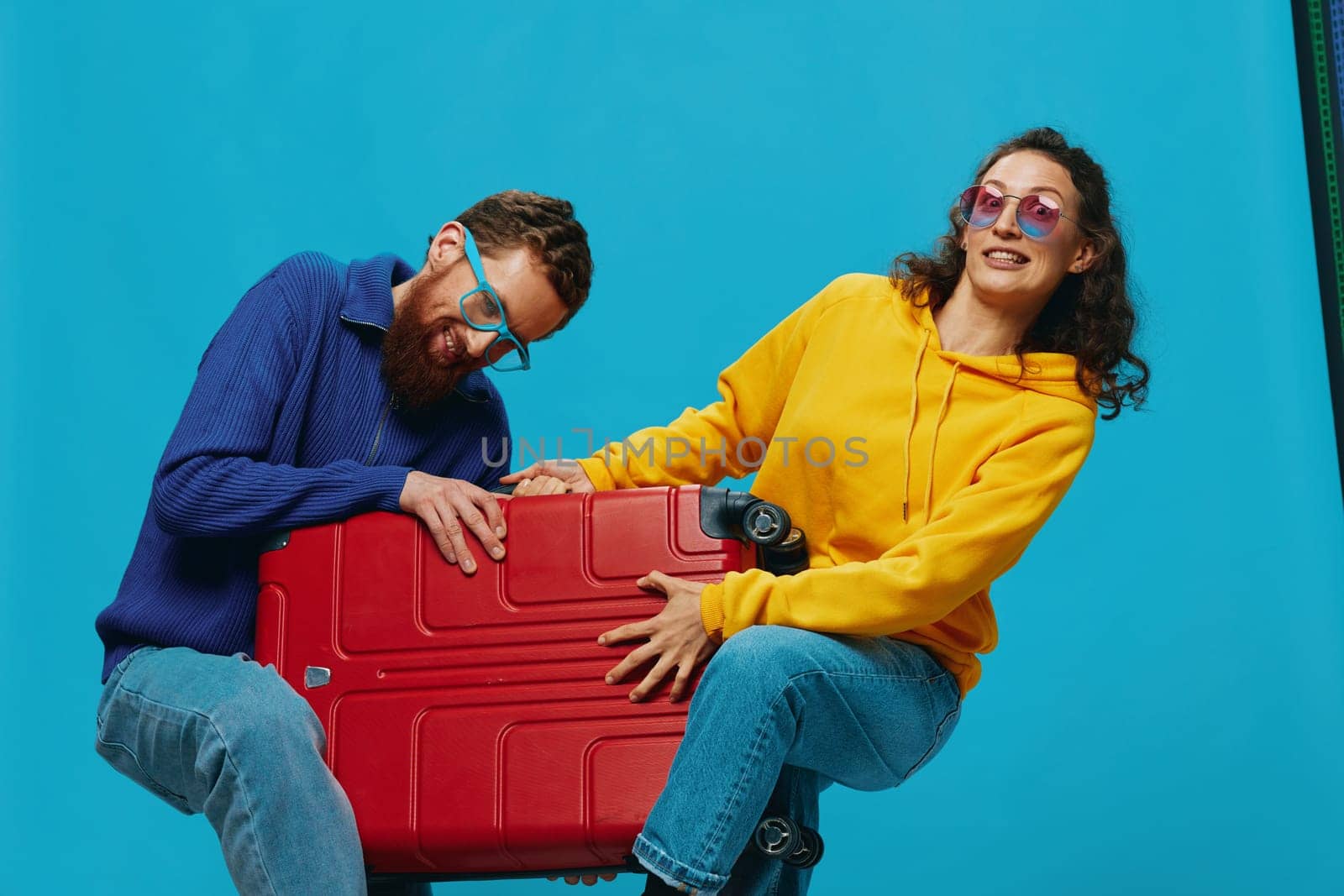 Woman and man smile suitcases in hand with yellow and red suitcase smile fun, on blue background, packing for a trip, family vacation trip. by SHOTPRIME